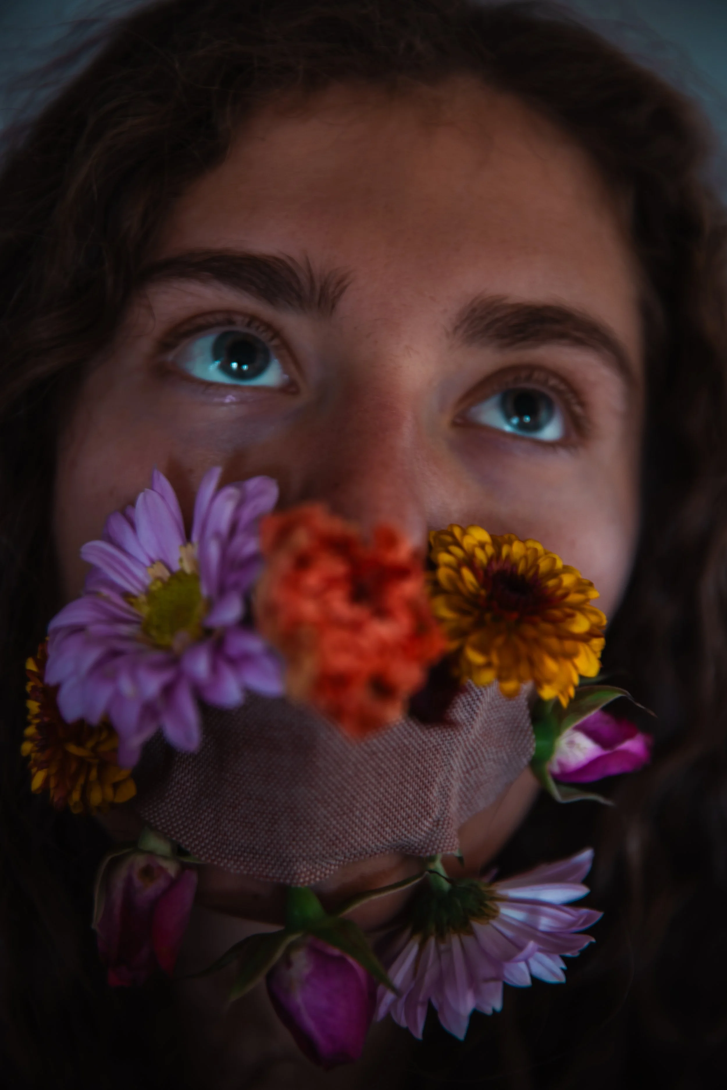 Close-up of a person's face with flowers covering their mouth, looking upwards.