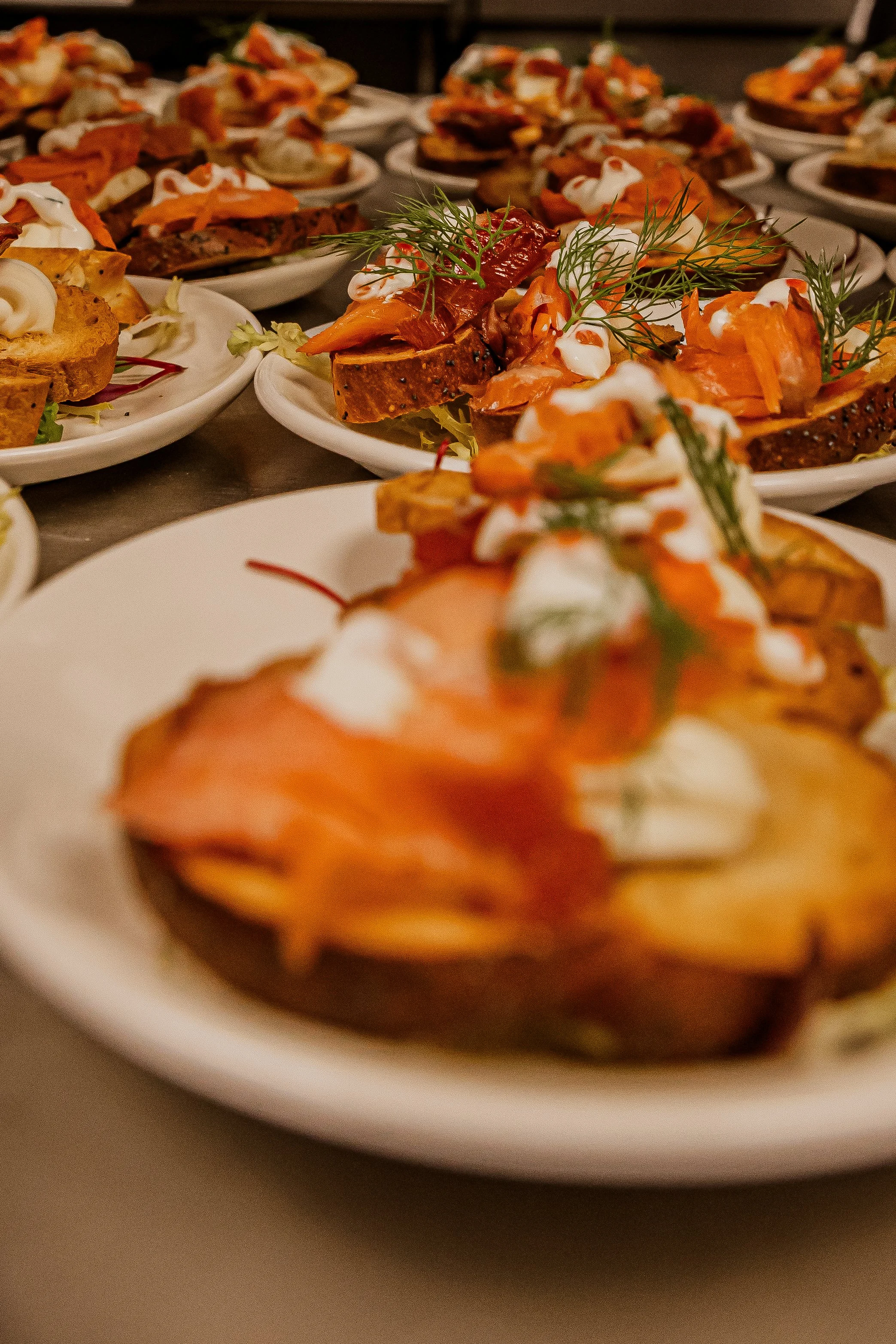 Multiple plates of smoked salmon crostini garnished with dill and drizzled with white sauce.