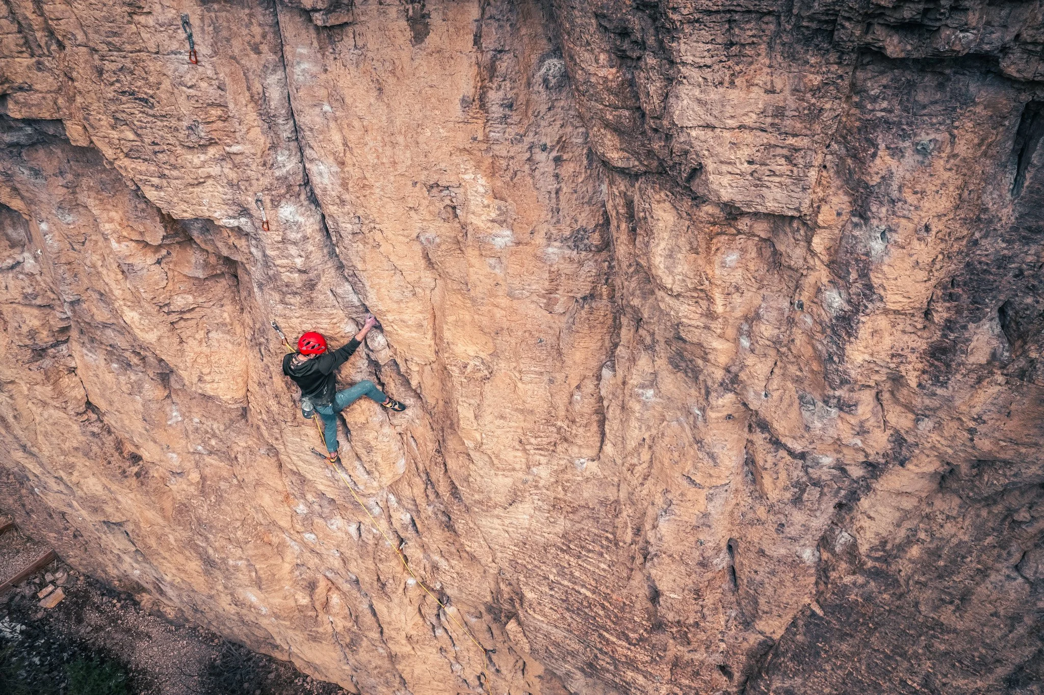 A person wearing a red helmet and climbing gear is ascending a steep, rugged rock face during rock climbing.