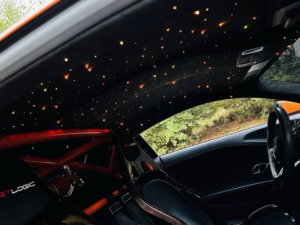 The interior of a race car with a starry sky ceiling projection and a red roll cage.