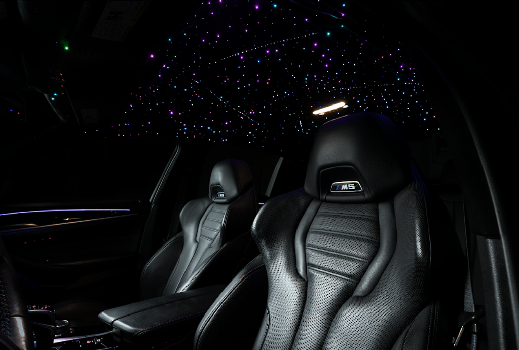 Inside a luxury car with black leather seats, featuring the BMW M5 logo, under a ceiling decorated with colorful star-like lights resembling a starry sky.
