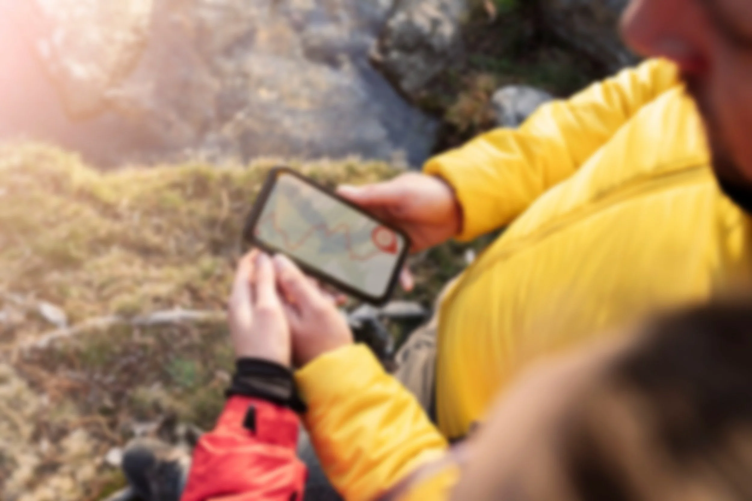 Person in yellow jacket looking at a smartphone with a map in an outdoor natural setting.
