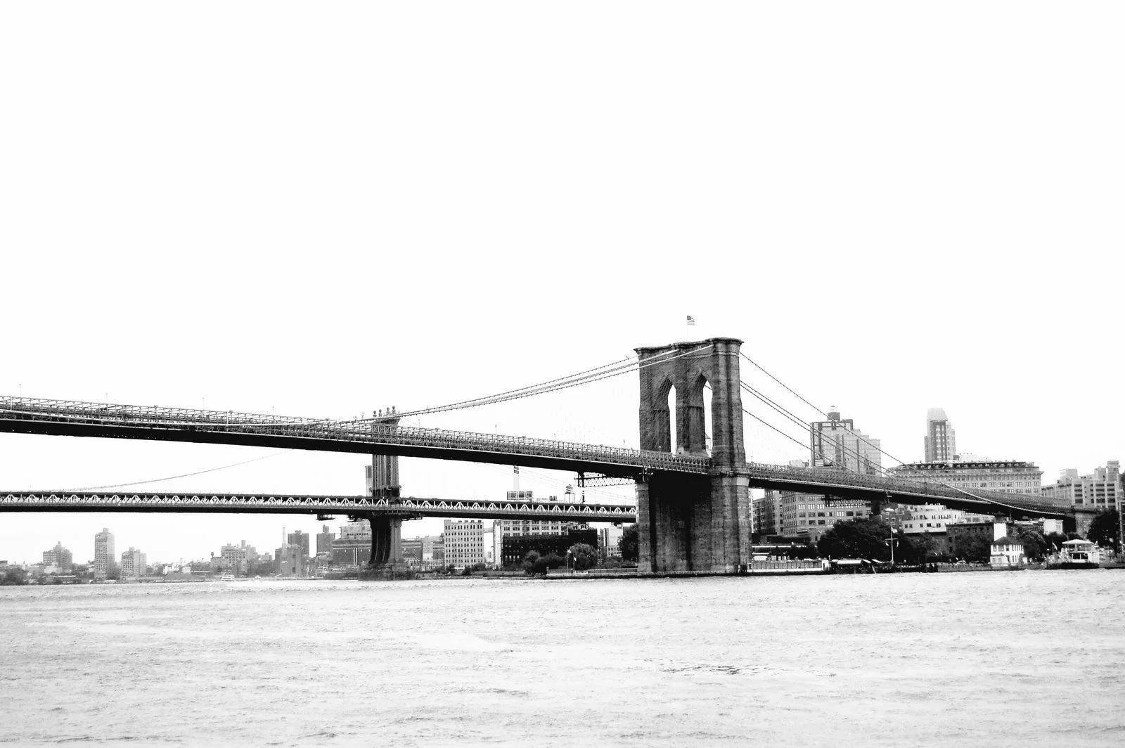 Black and white photo of the Brooklyn Bridge spanning the East River, with New York City skyline in the background.