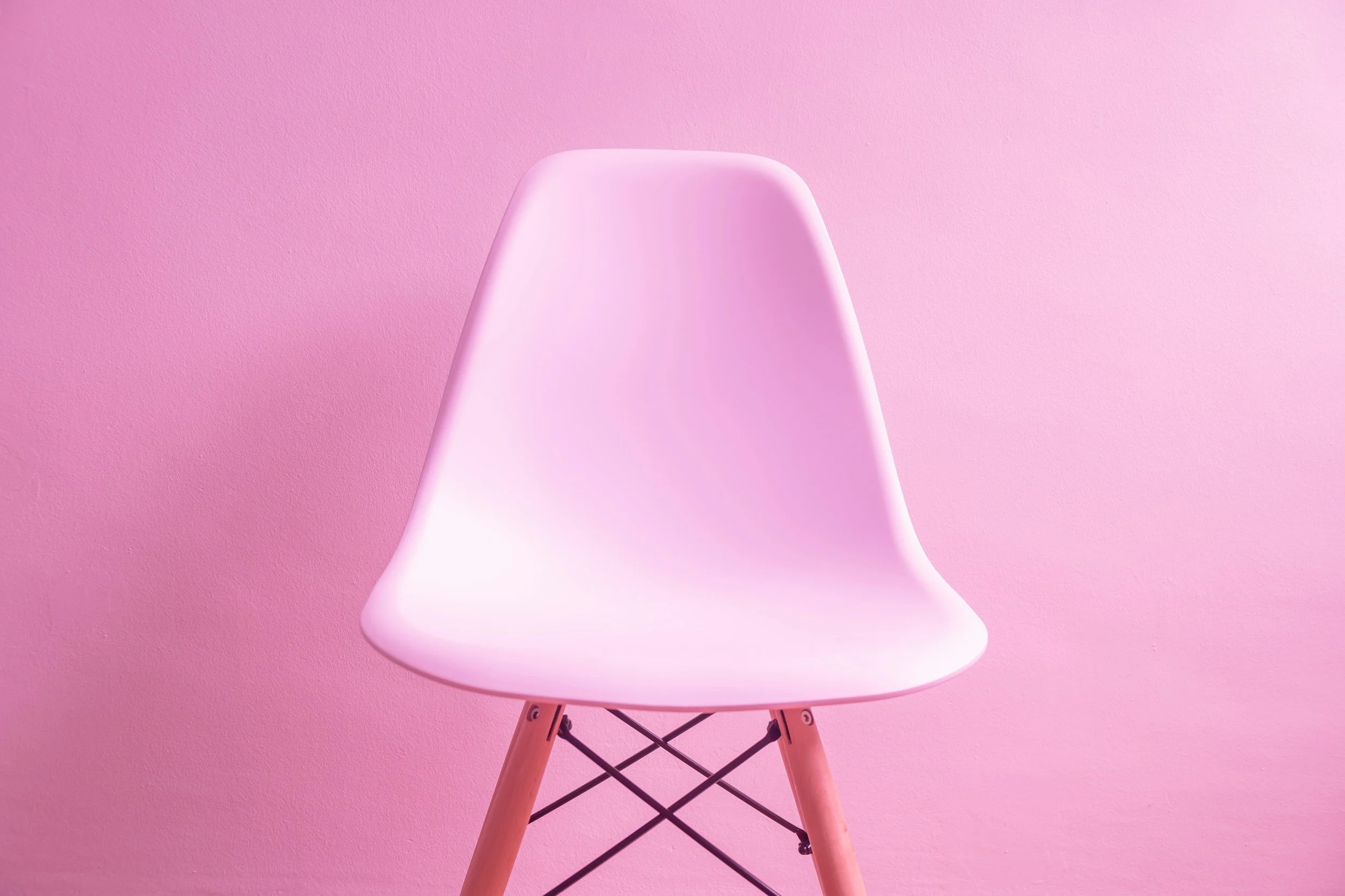 A pink modern chair with wooden legs against a pink wall.