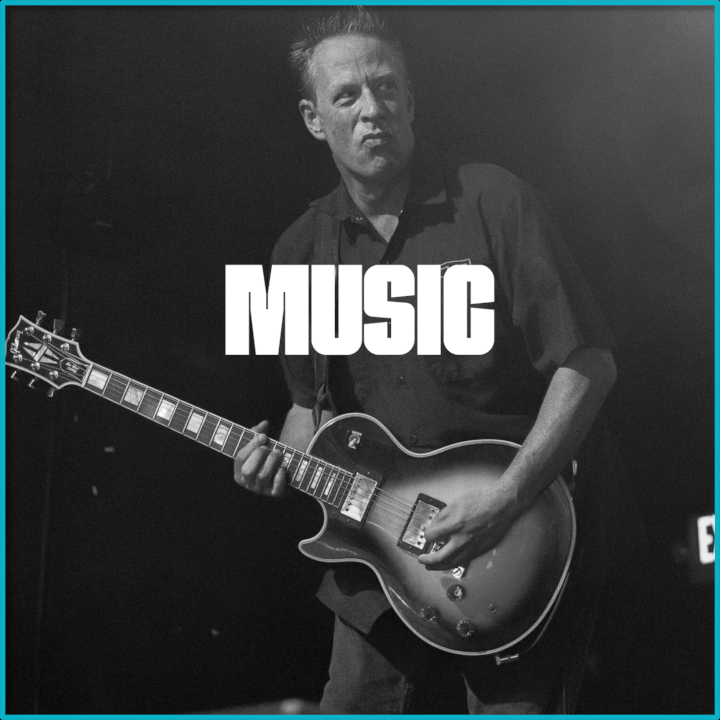 A man playing an electric guitar on stage with the word 'MUSIC' overlayed in bold white letters.