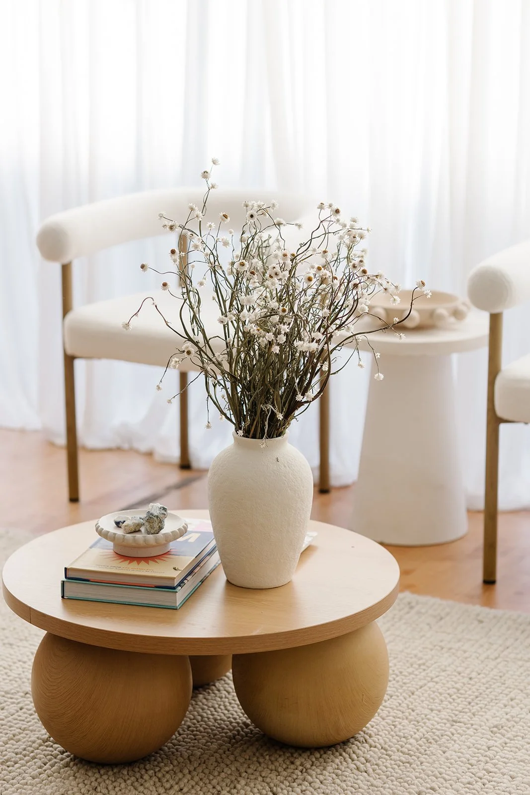 The entrance and waiting area of See Pilates. A round coffee table with flowers in a vase and two chairs are in the background, and sheer white curtains.