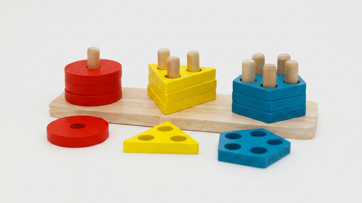 A wooden sorting toy with red circles, yellow triangles, and blue squares arranged on pegs.