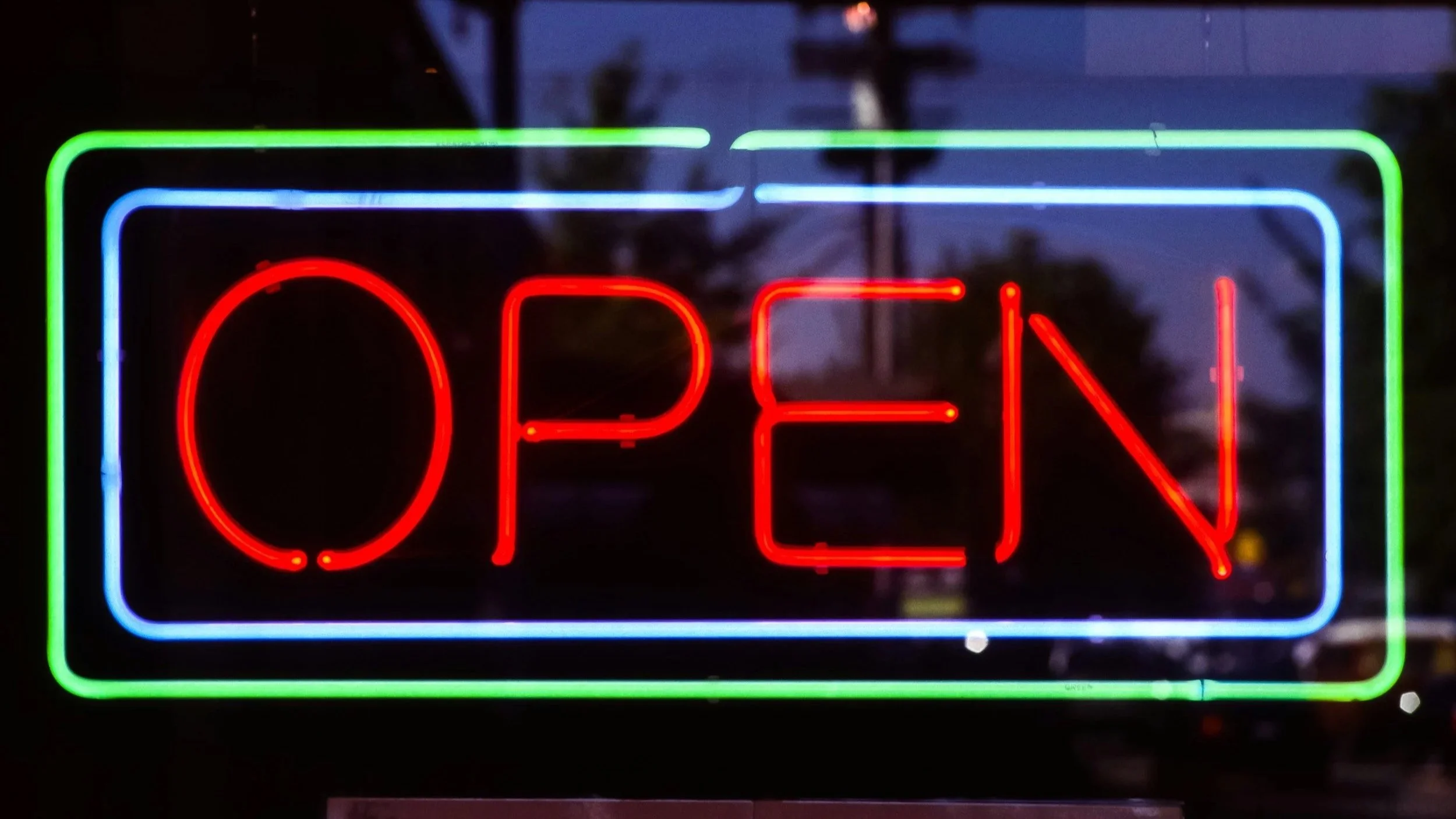 Neon “OPEN” sign glowing in a window at night, symbolizing emotional openness and availability.
