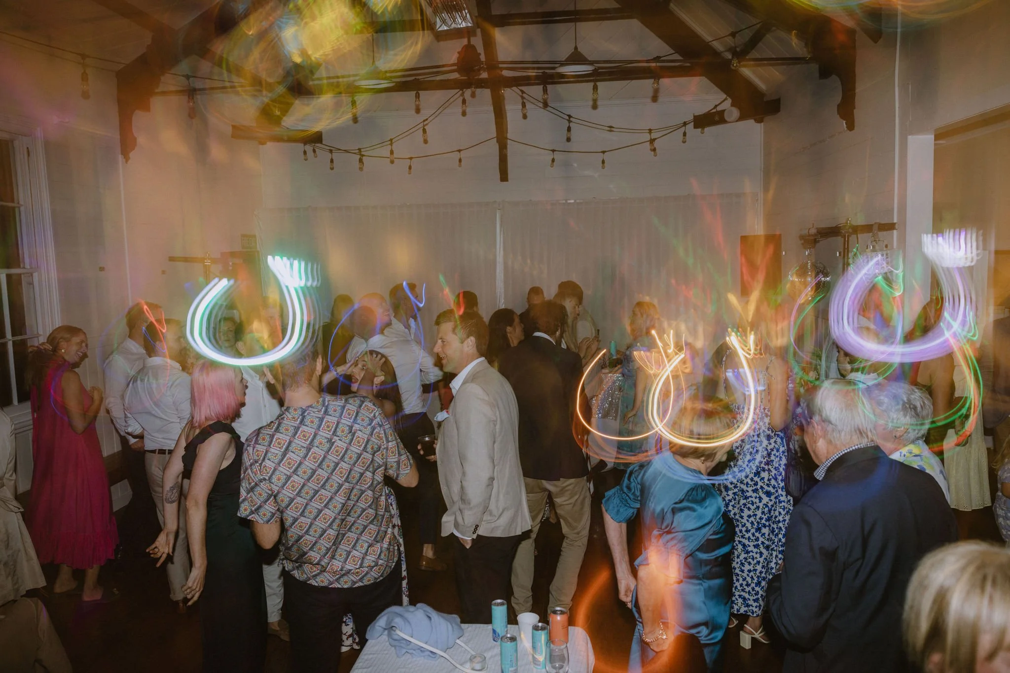 People dancing and socializing at a party with colorful lights and a wooden ceiling.