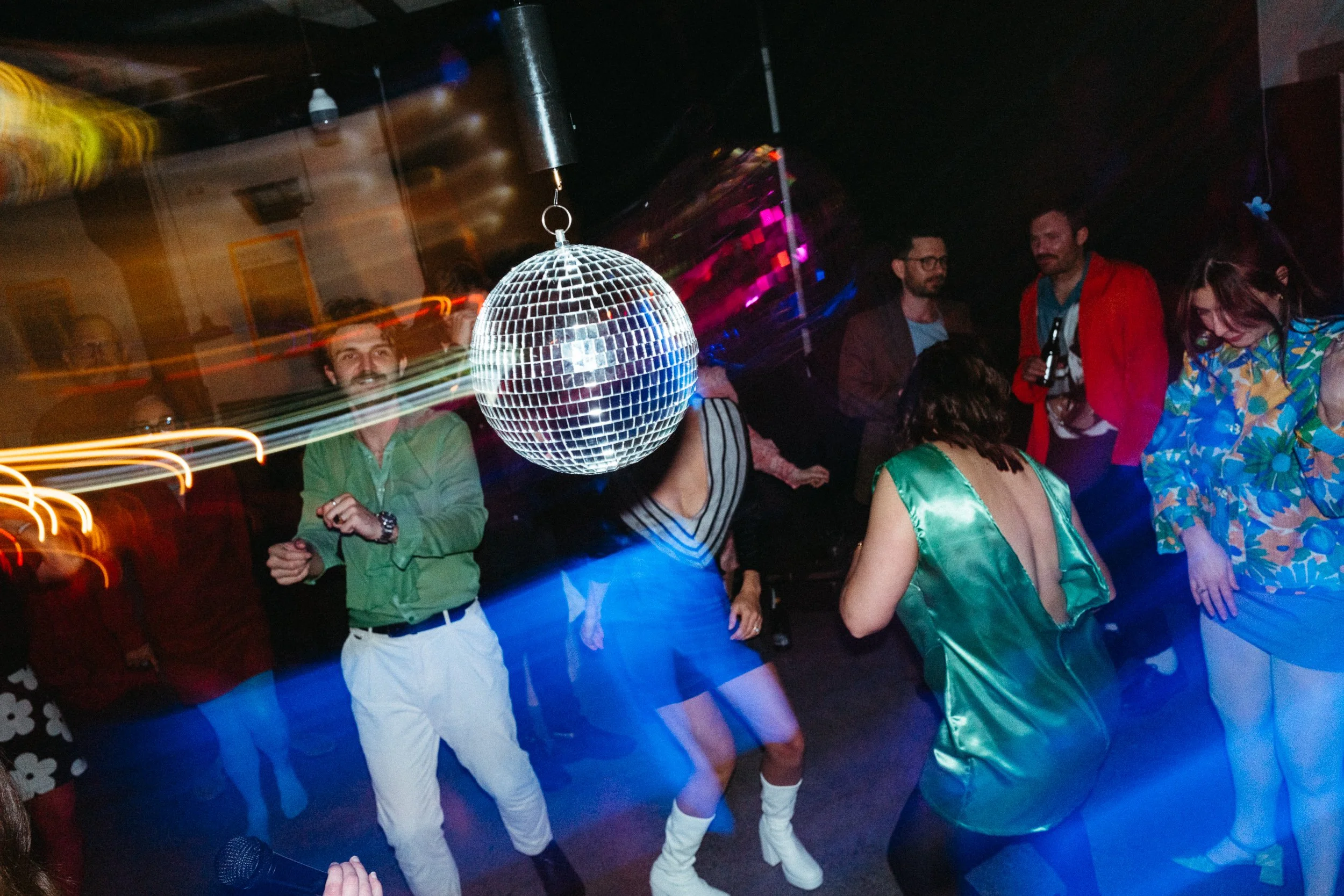 People dancing around a disco ball in a nightclub with colorful lights.