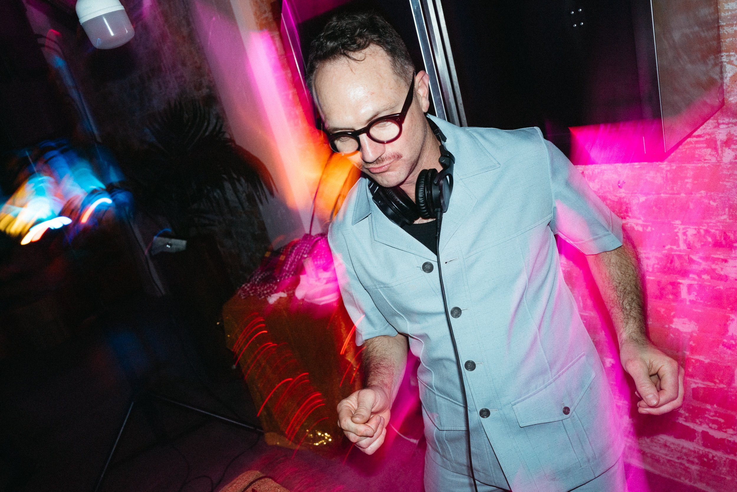 A man wearing glasses and earphones dancing at a party with colorful lights and blurred motion effects.