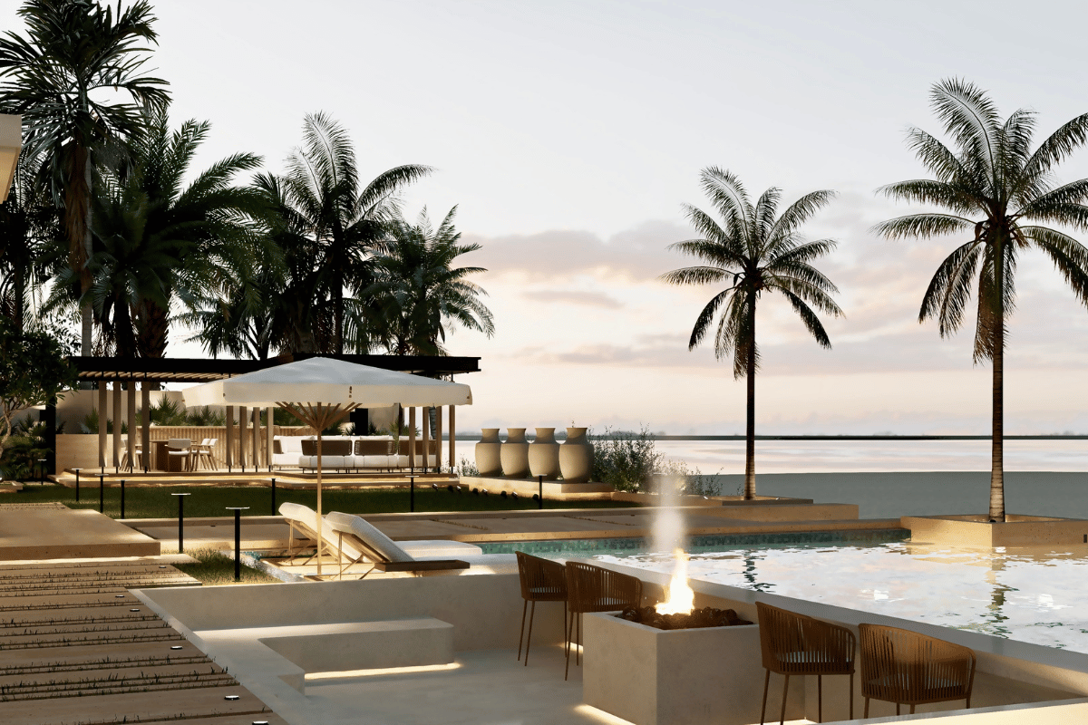 Luxury outdoor pool area with lounge chairs, umbrella, fire pit, and palm trees overlooking water at sunset.