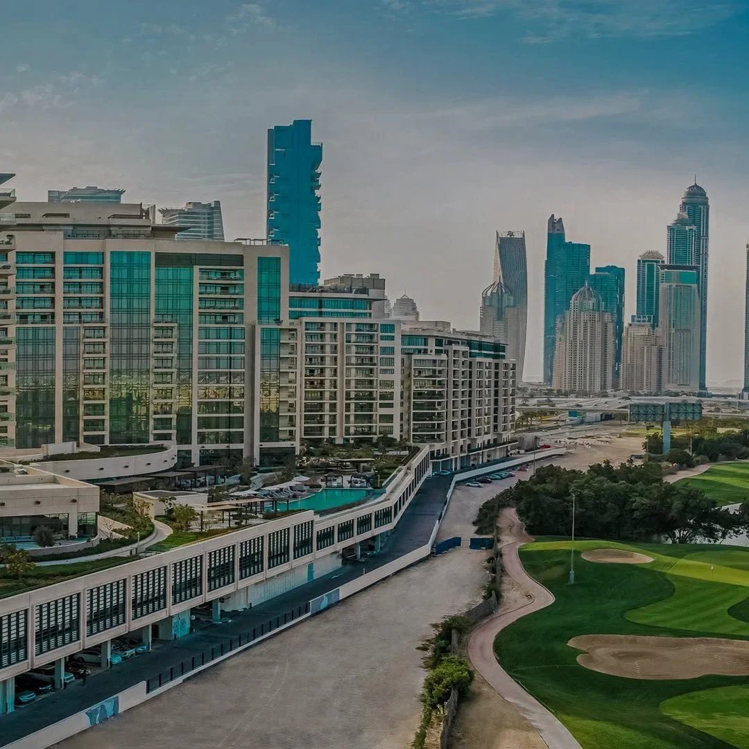 A cityscape with tall modern skyscrapers, a building with blue glass windows, a parking garage, and a golf course with green grass and sand traps.