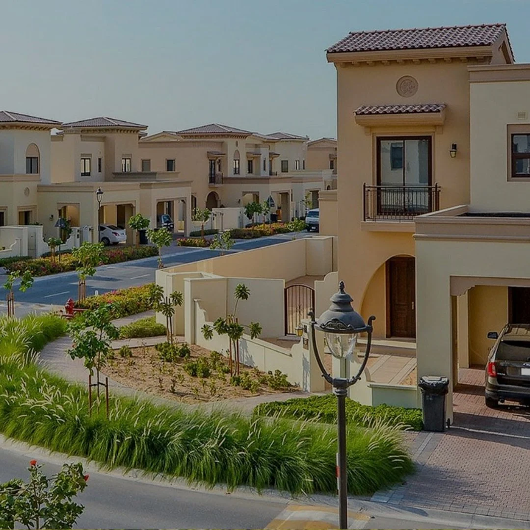 A modern residential neighborhood with beige houses, small trees, well-maintained lawn, and street lamps.