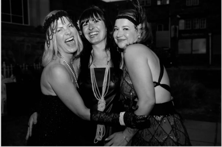 Three women in vintage 1920s flapper costumes, smiling and having fun at a party.