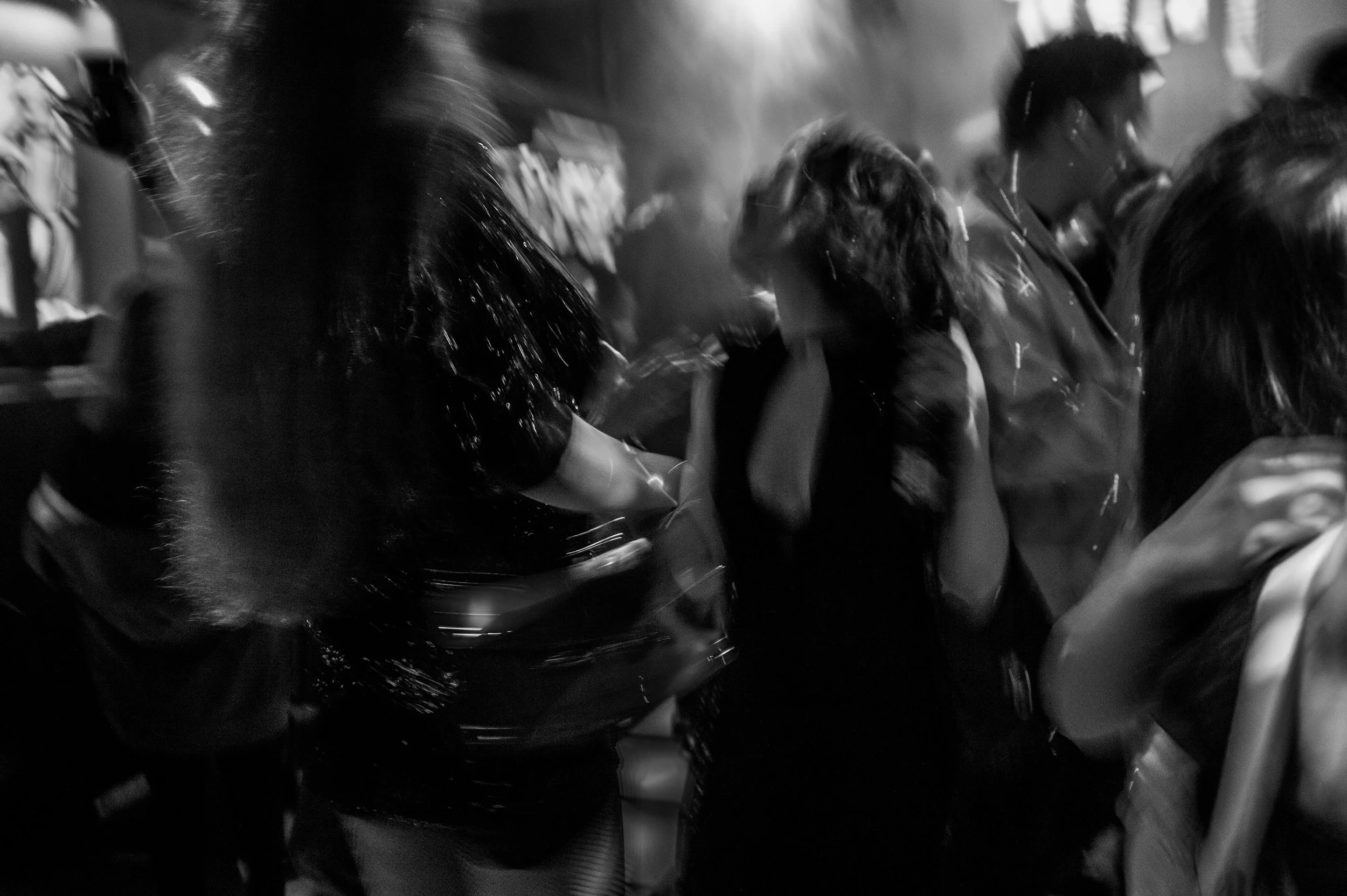 Blurred black and white photo of people dancing in a crowded club or party.