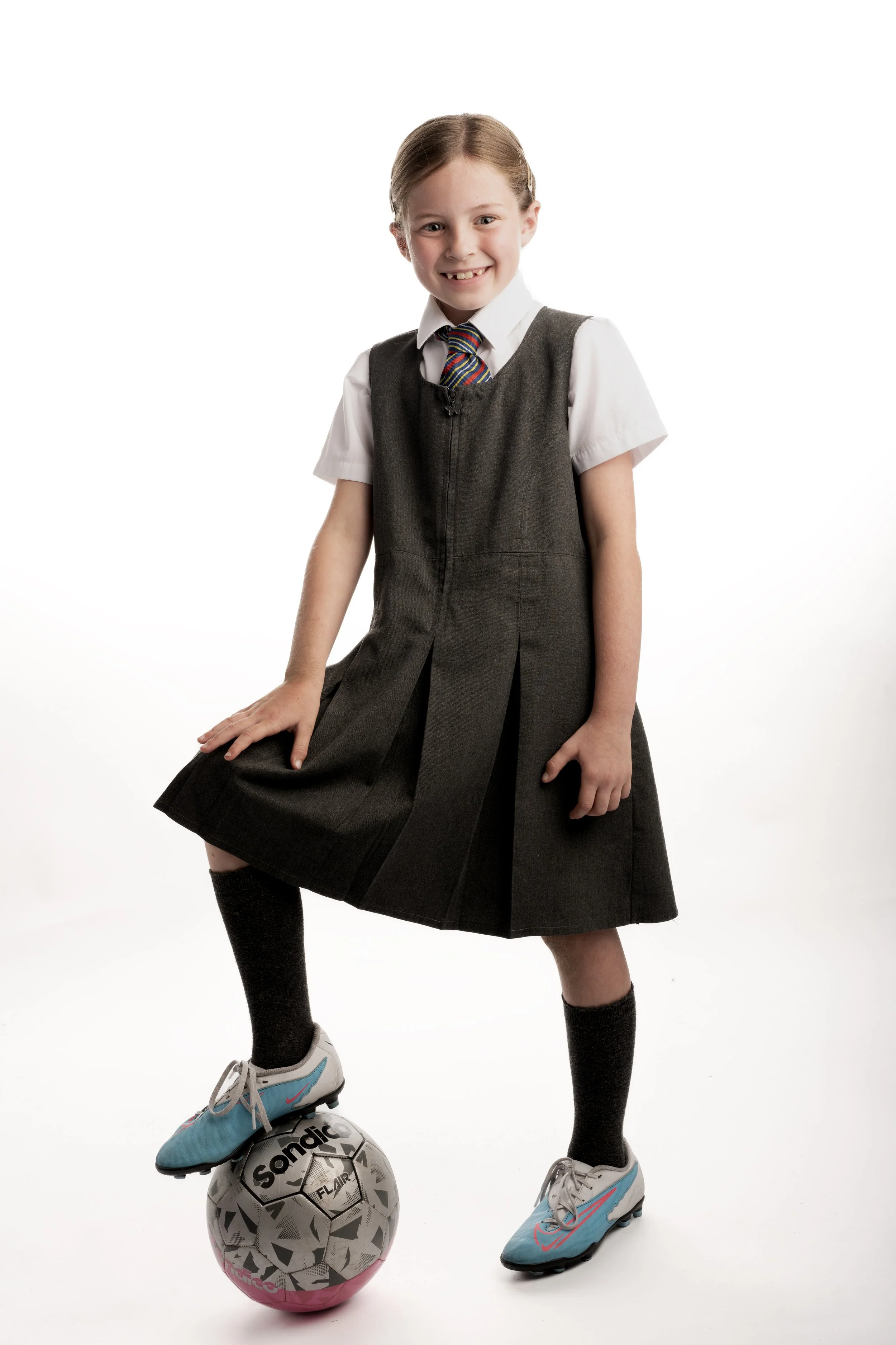 Child in school uniform with blue soccer cleats standing on a soccer ball.