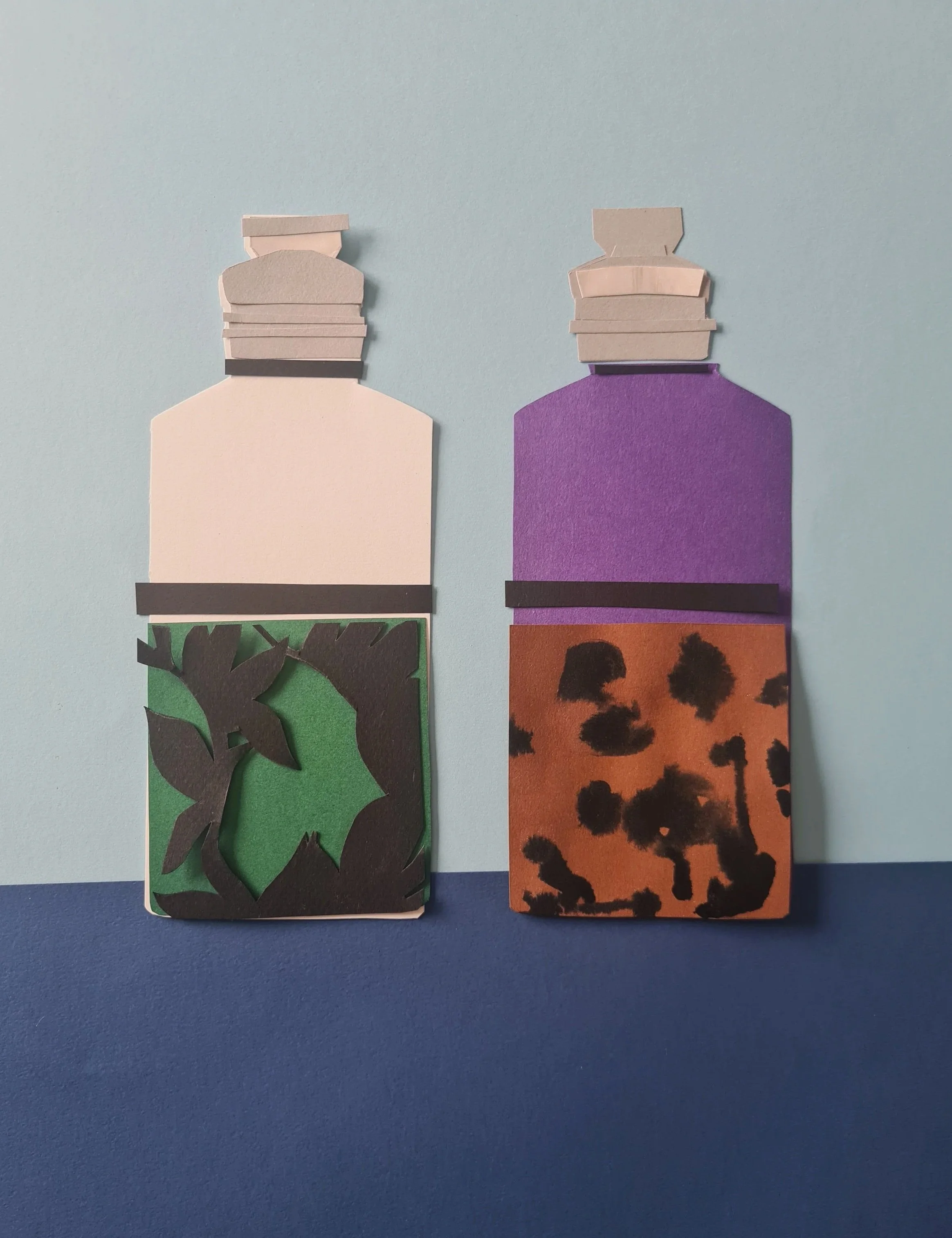 Two paper bookmarks with illustrated animal silhouettes and backgrounds, one featuring trees and another featuring animal print, placed on a blue surface.