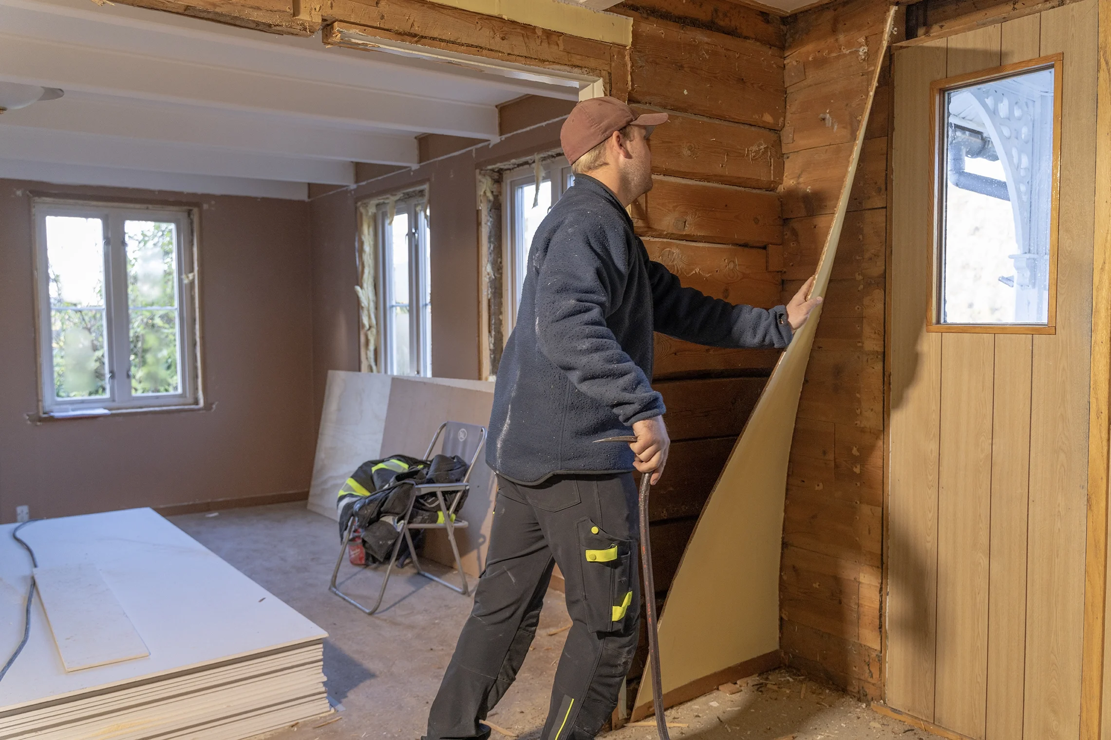 A man working on interior renovation of a house, installing drywall on a wooden wall
