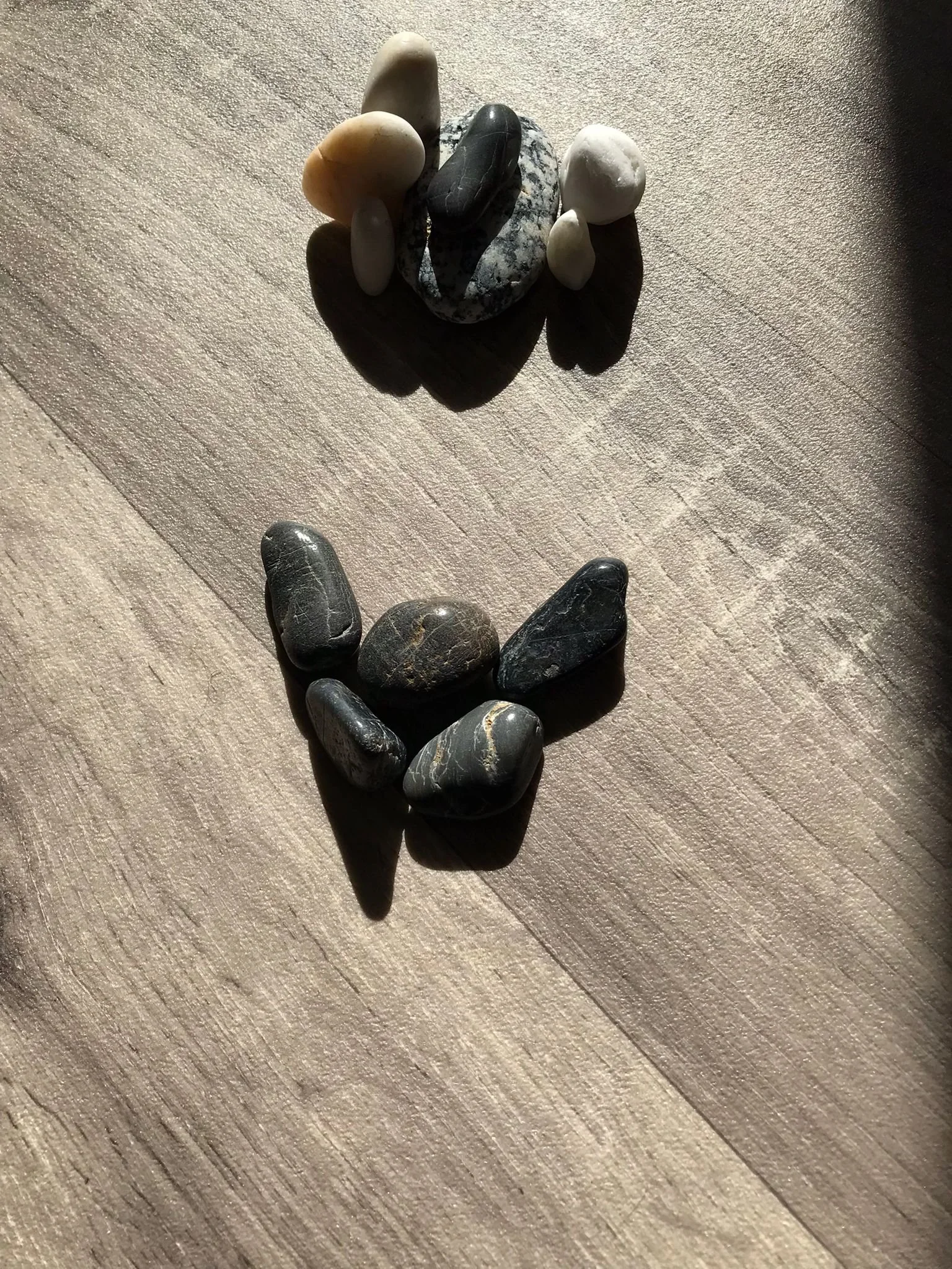 Collection of small stones and pebbles arranged on a wooden surface with sunlight casting shadows.