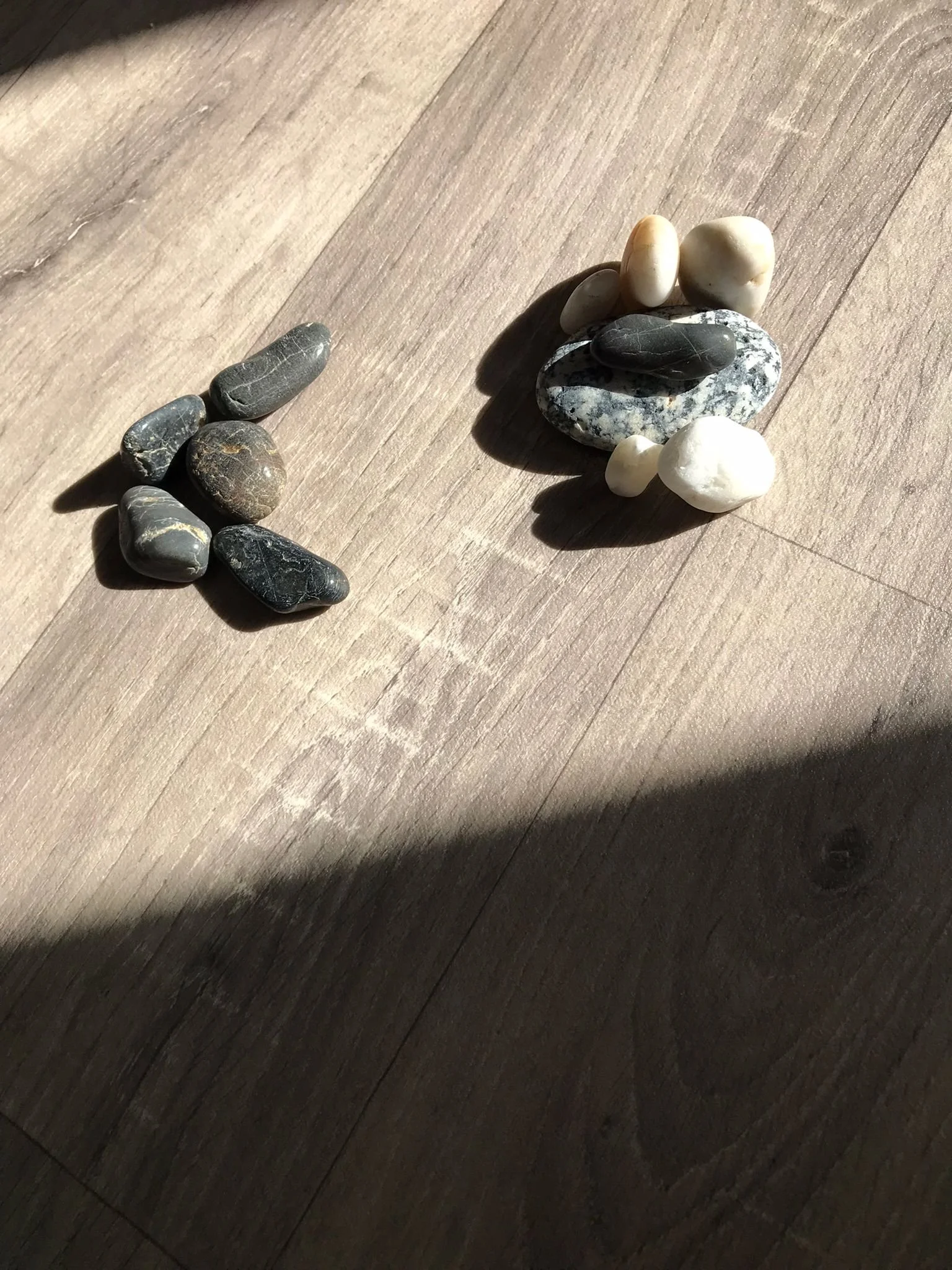 Collection of smooth stones arranged on a wooden surface, with sunlight casting shadows.