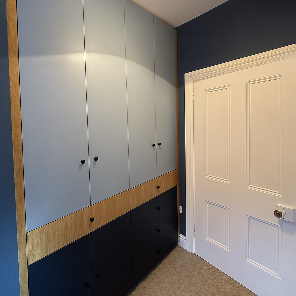 Vertical built-in storage cabinets in shades of blue, wood, and black next to a white paneled door in a room with dark blue walls and beige carpet.