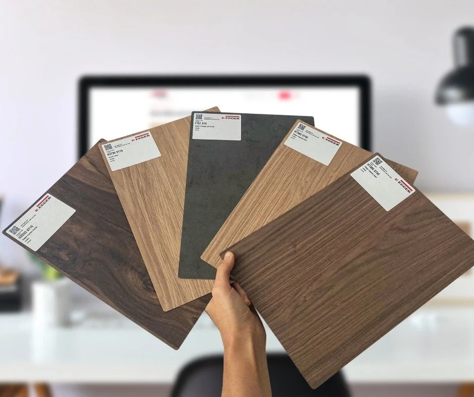 Person holding five wood or laminate flooring sample boards in front of a computer monitor.