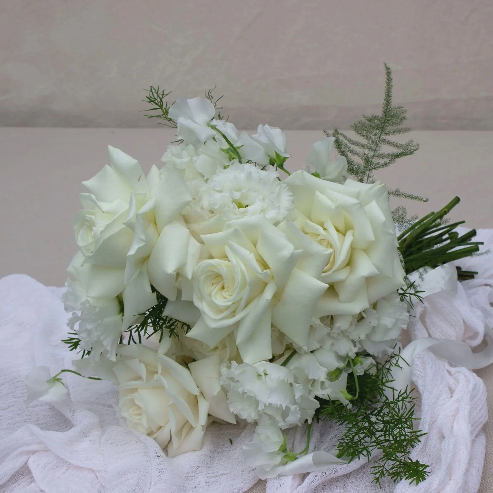White floral bouquet including roses and other white flowers with green foliage, resting on white fabric