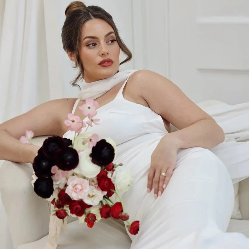 bride in a luxury white dress and sheer scarf, holding a pink, white, red and burgundy bridal bouquet of ranunculus and roses