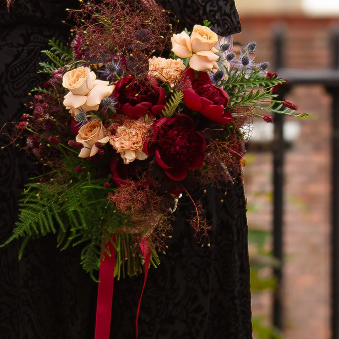 Gothic bride, in a black wedding dress, carrying a red, peach and burgundy bridal bouquet, for a June wedding in Norwich city