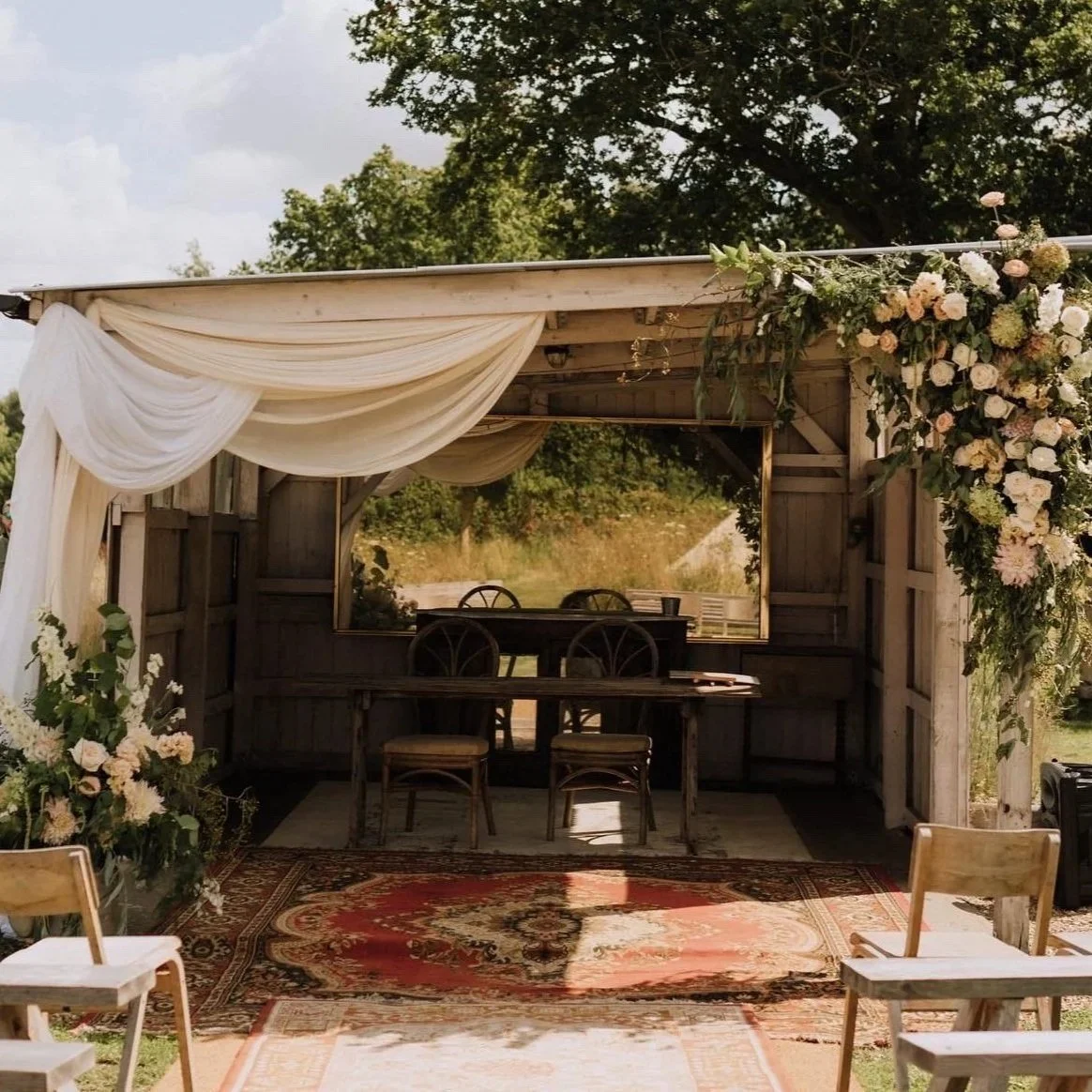 Norfolk countryside wedding ceremony set up, with a large floral installation on a wooden structure and soft draping fabrics