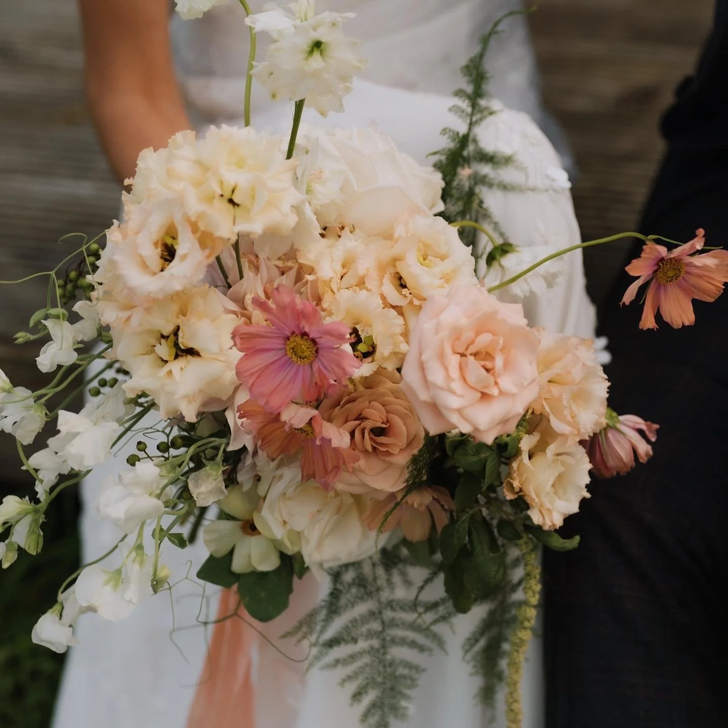 Pastel pink, peach, cream and green summer bridal bouquet for a countryside Norfolk wedding, held by a bride in a white dress