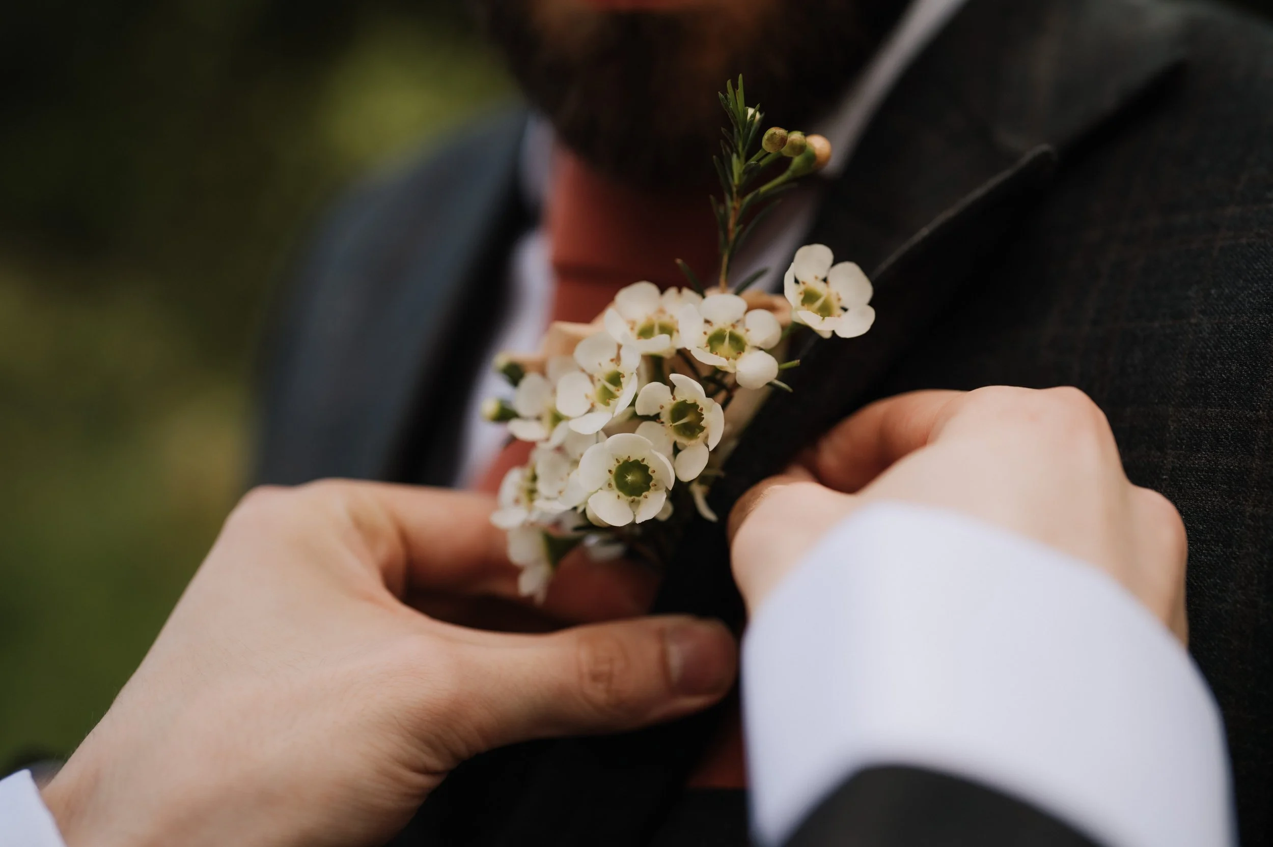 Person pinning a white flower boutonniere onto a man's suit jacket.