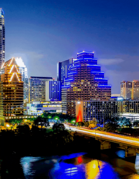 Austin skyline at night with illuminated buildings and bridge.