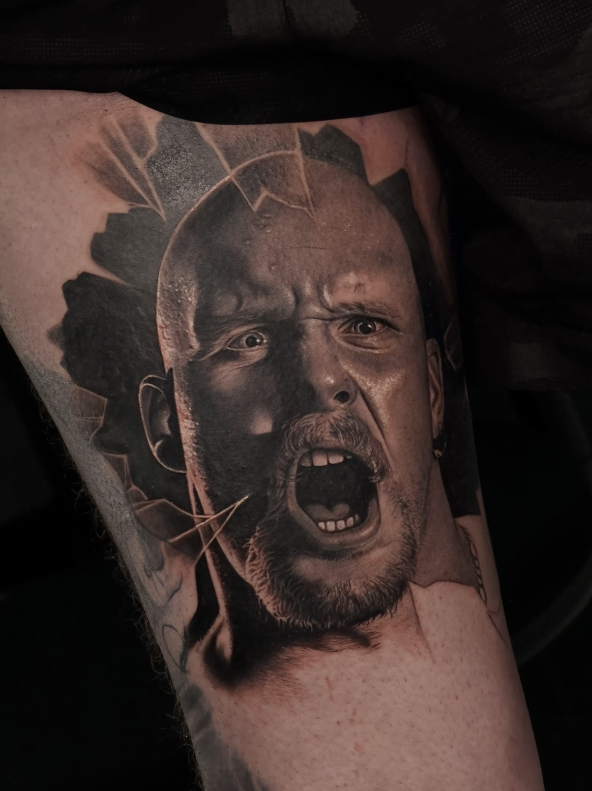 A tattoo of a person's face with an intense expression, mouth open, showing teeth, and eyes wide open.