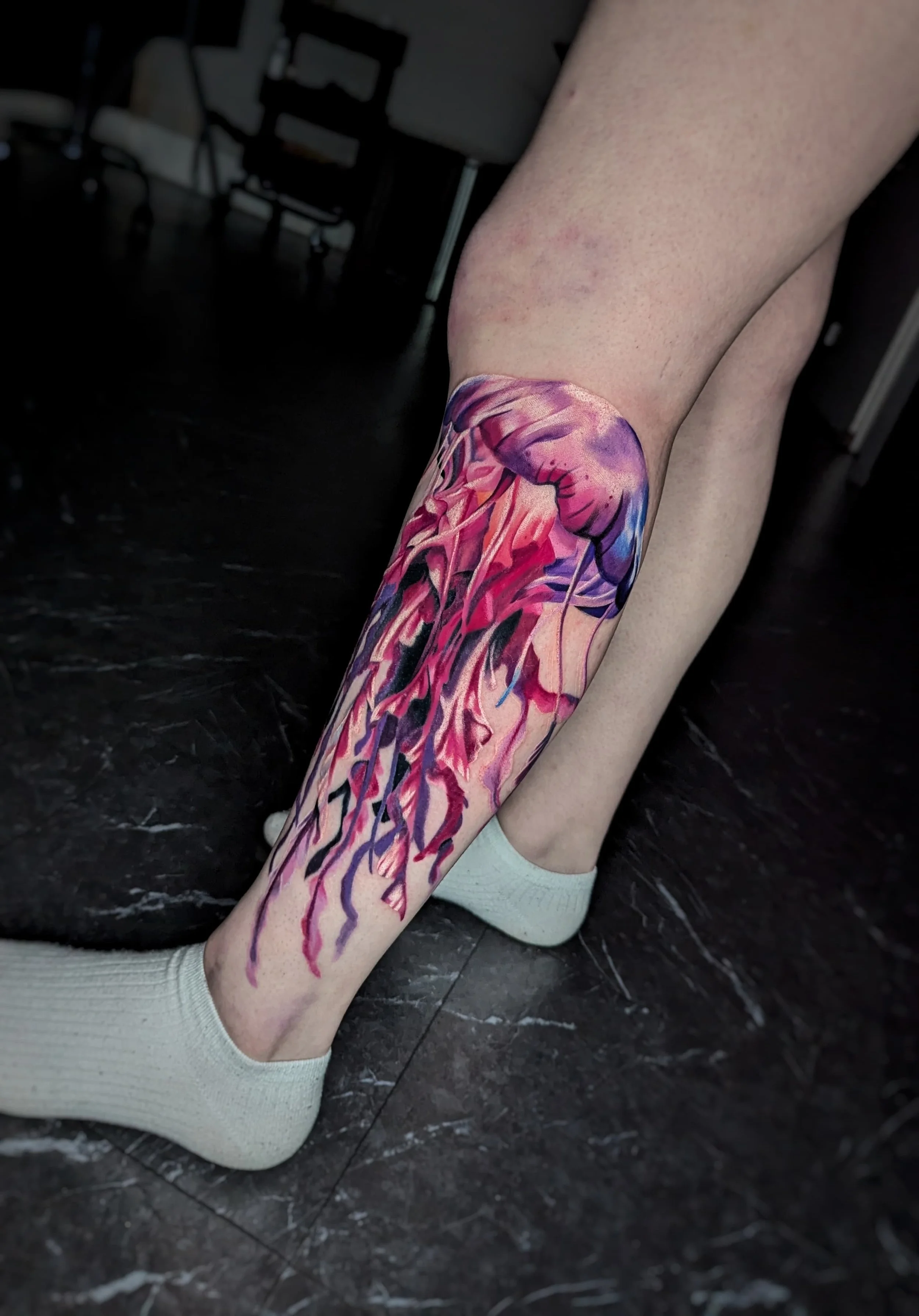 Colorful jellyfish tattoo on person's lower leg and ankle.