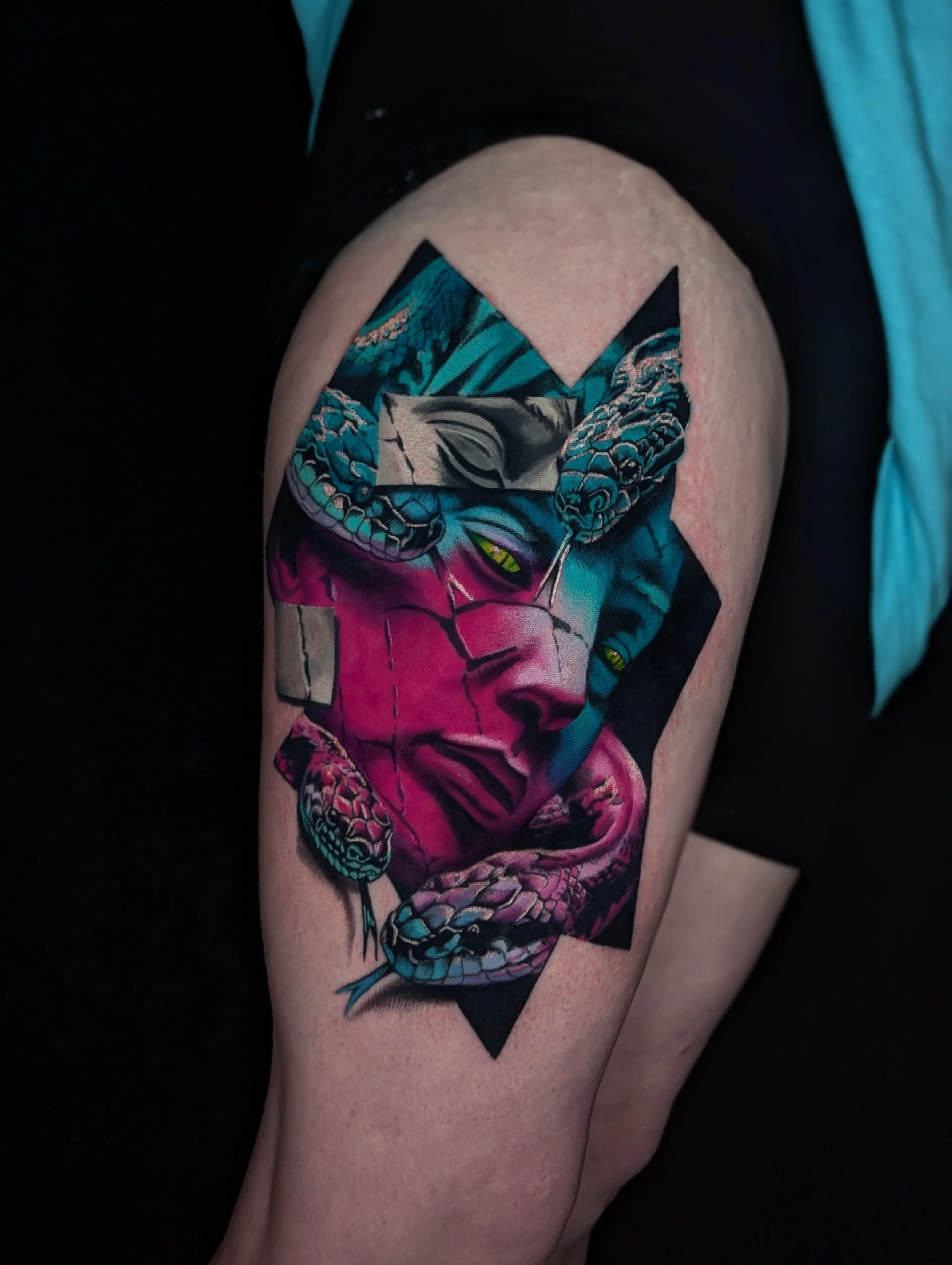 Colorful tattoo of a woman's face with snakes intertwined, set against a geometric black background on a person's thigh.