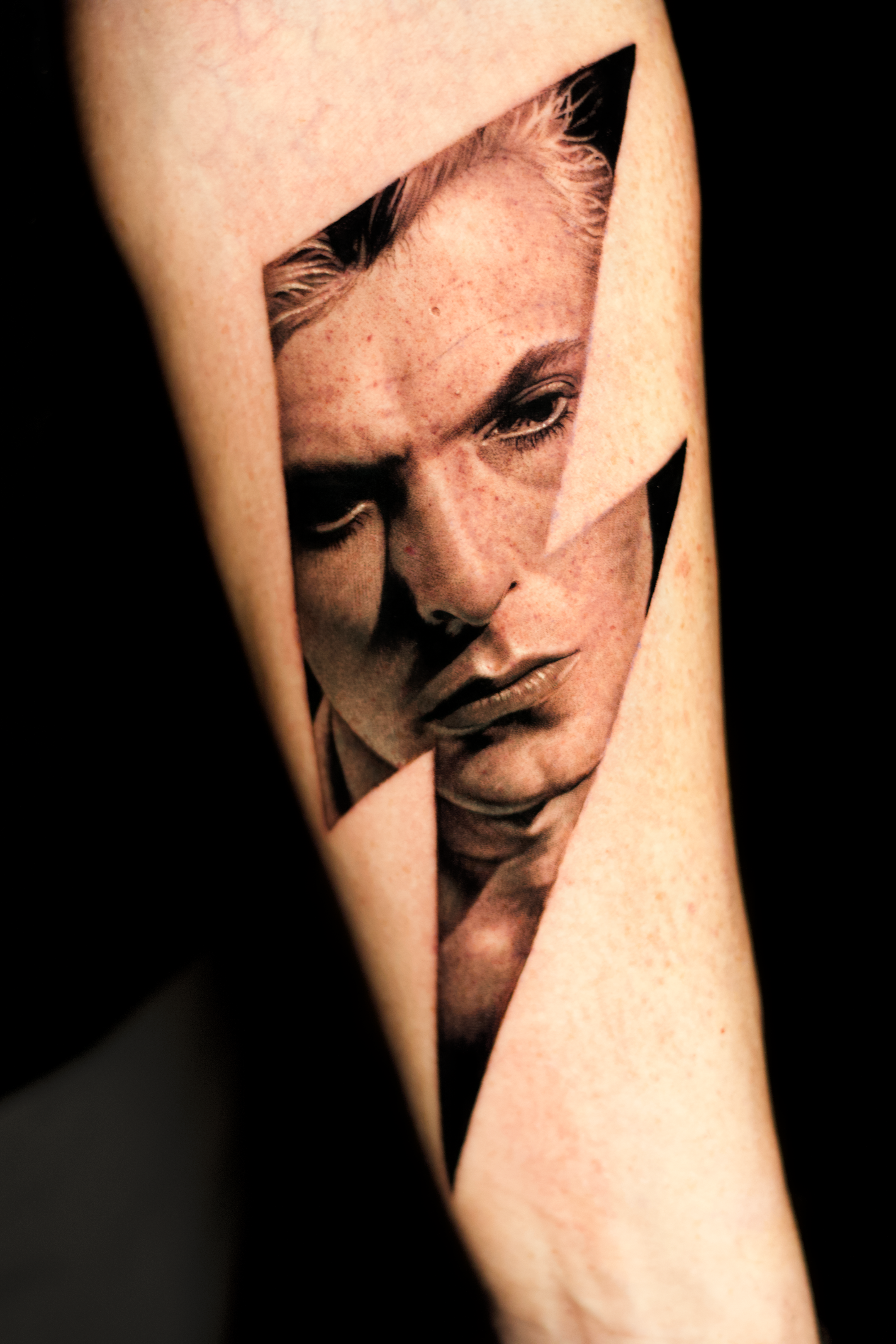 Close-up of a tattoo of a woman's face on someone's arm, showing detailed shading and skin texture.