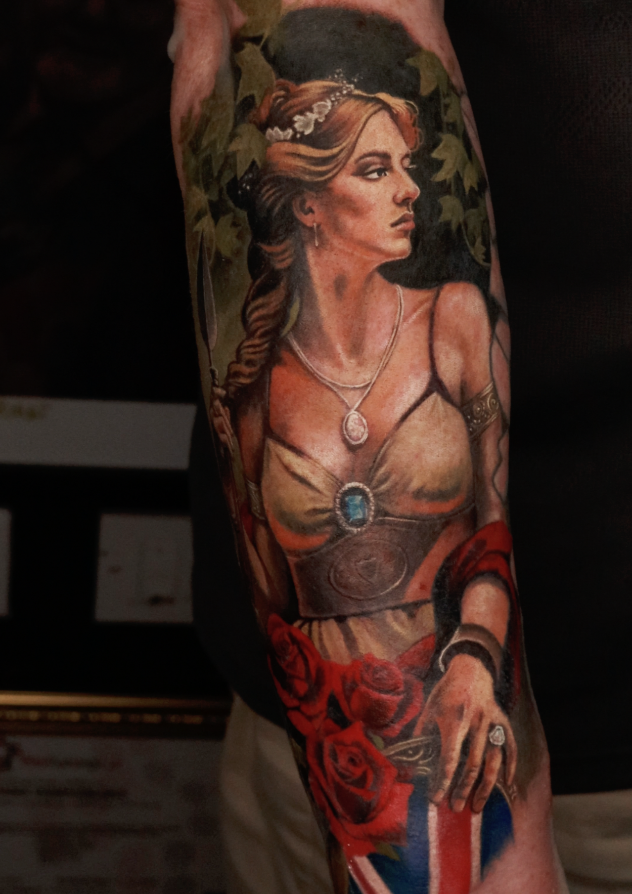 Colorful tattoo sleeve featuring a woman with long wavy hair, wearing jewelry, a dress, and holding red roses, with a black background.