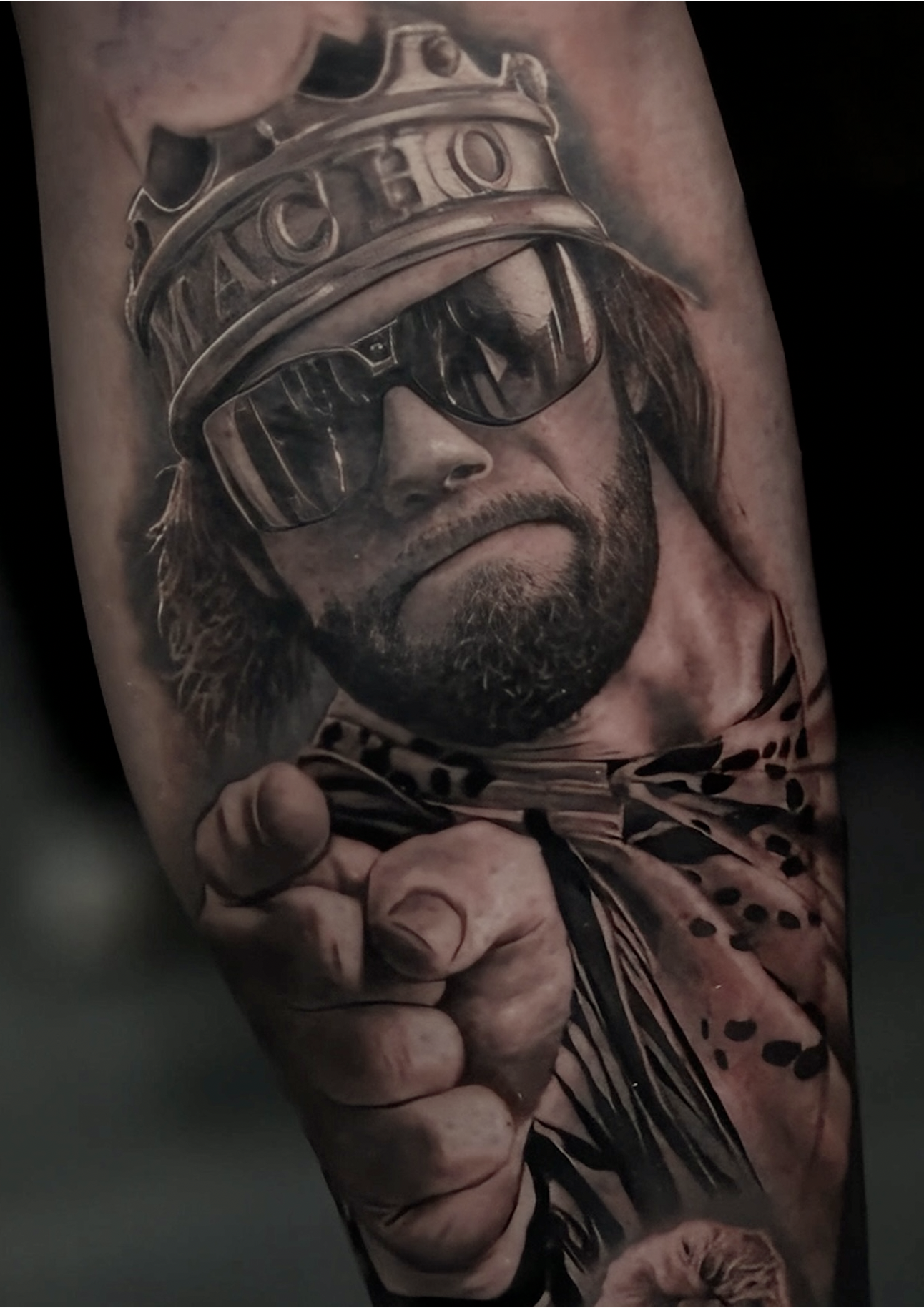 Black and gray realistic tattoo of a man with a beard and long hair wearing sunglasses and a hockey helmet, pointing directly at the viewer.