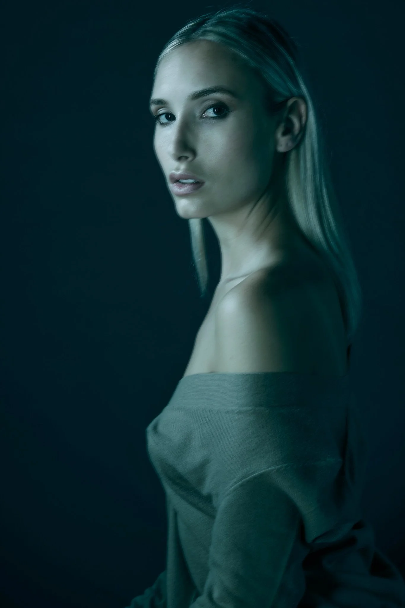 Retrato de una mujer con cabello rubio y ojos claros, vestida con una blusa gris, en un fondo oscuro.