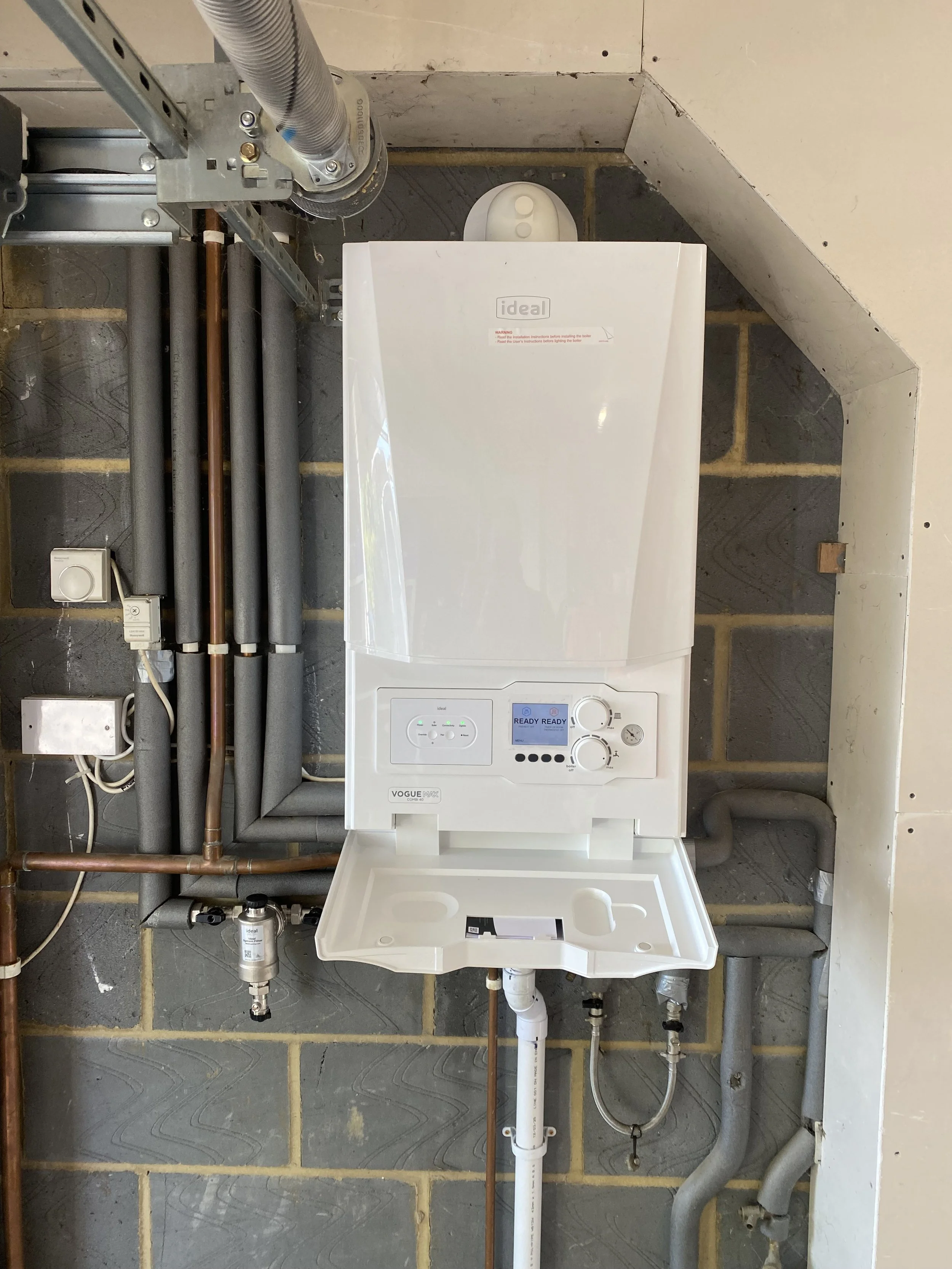 Utility area with a wall-mounted boiler, various pipes, and electrical connections.