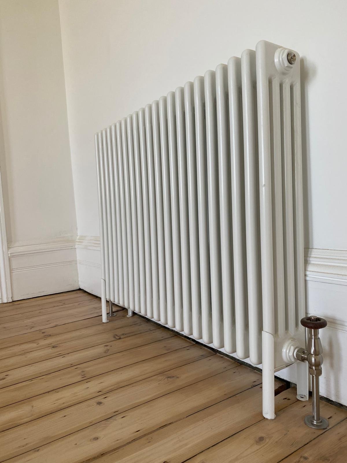 White radiator plumbed above wooden floor
