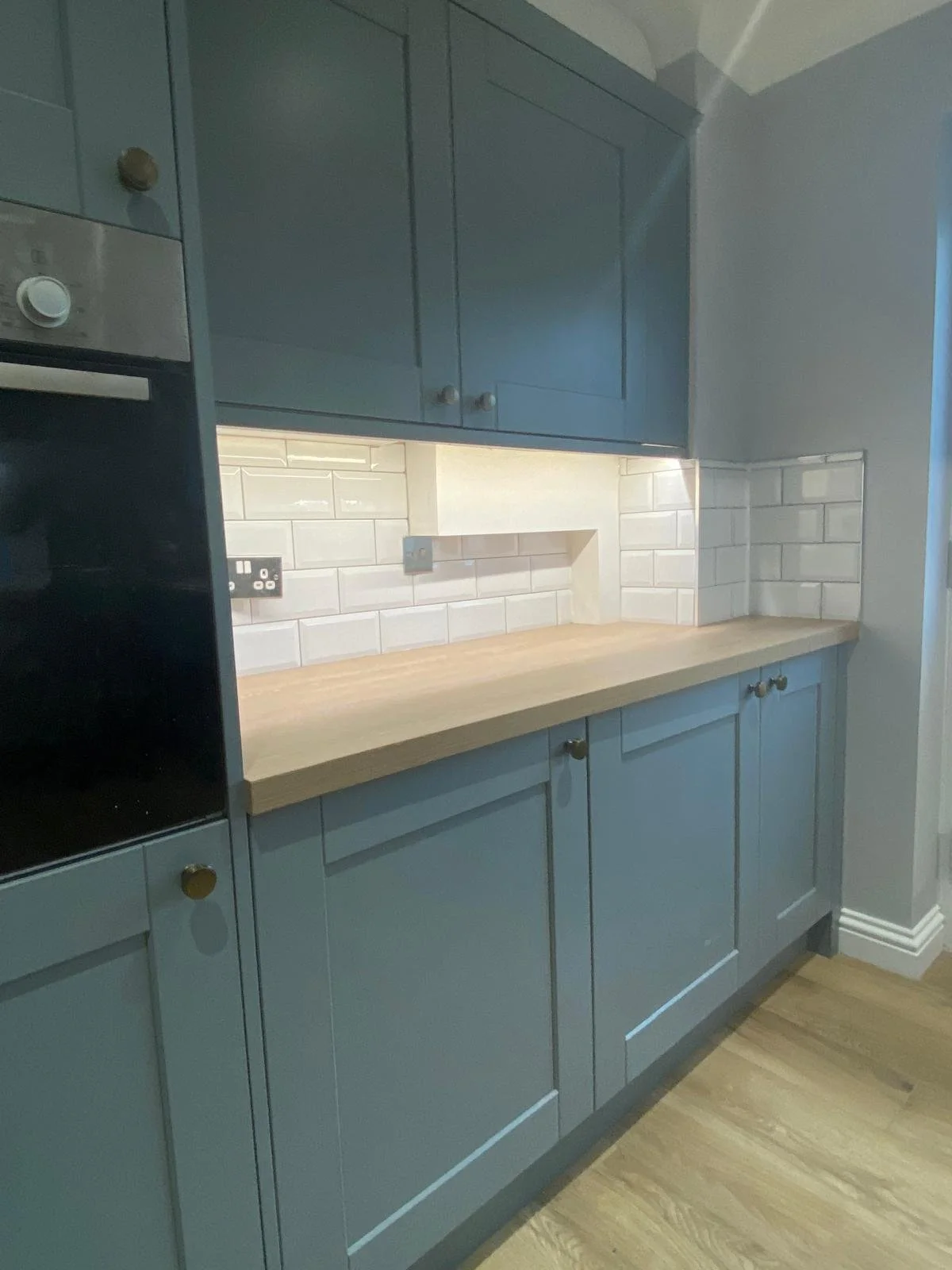 Kitchen with blue cabinets, white subway tile backsplash, wooden countertop, and hardwood floor.