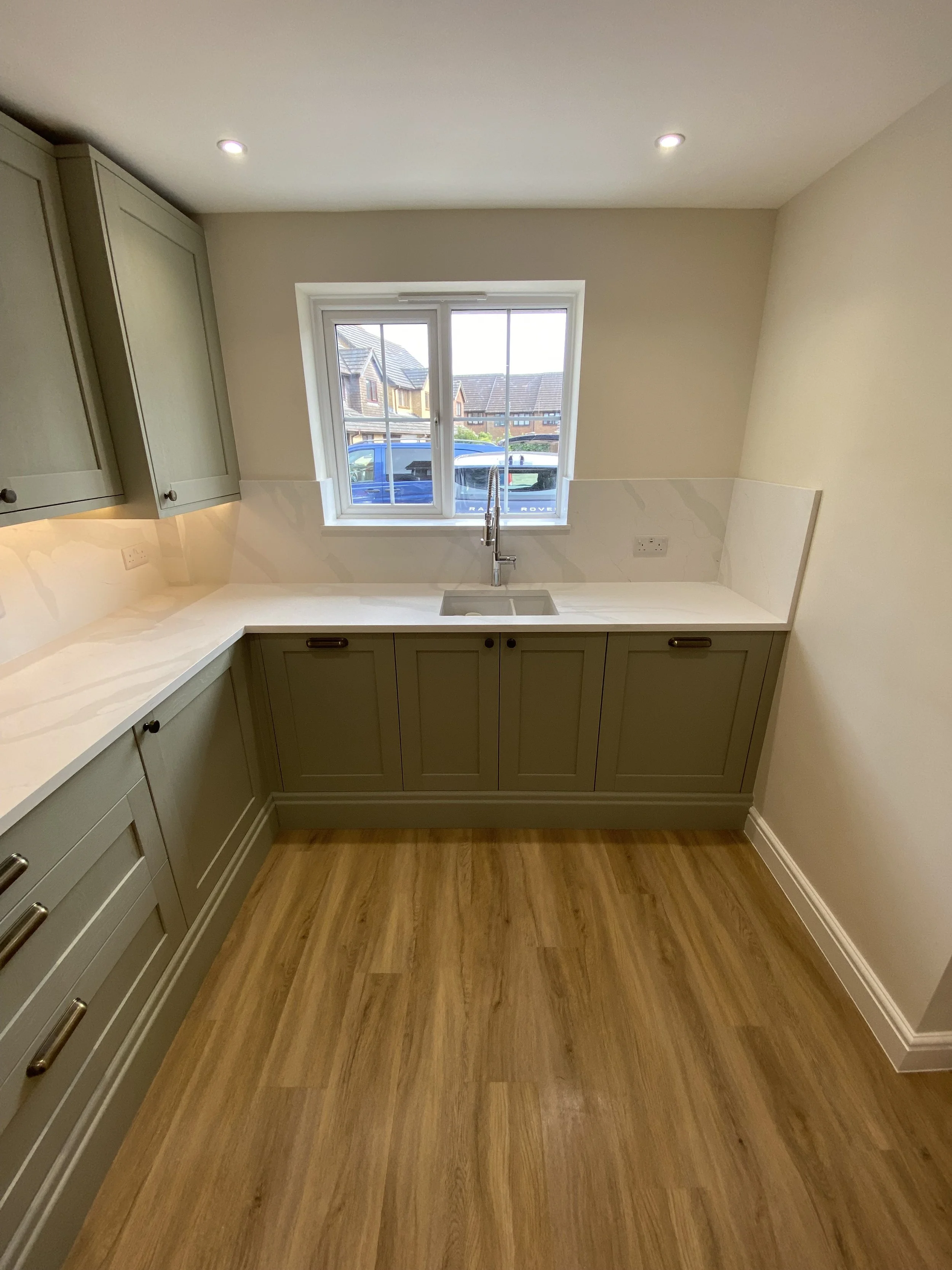 Kitchen with beige cabinets, marble countertops, a window above the sink, and wooden flooring.