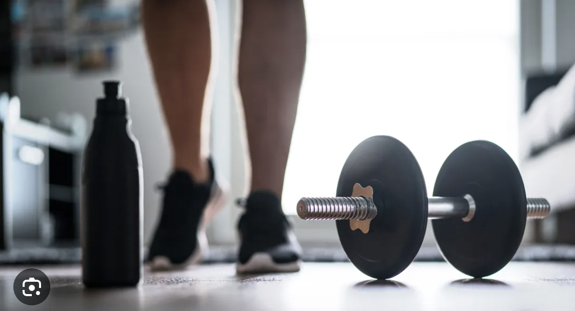 Close-up of yellow running shoes, a black dumbbell, and an SOS fitness weight plate in a gym.