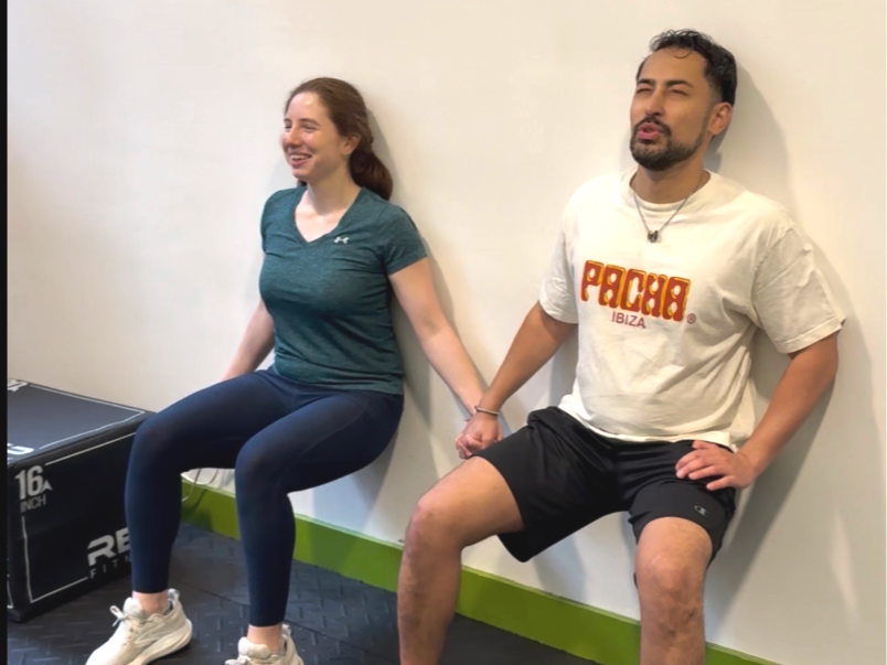 A couple holding hands while doing a wall-sit
