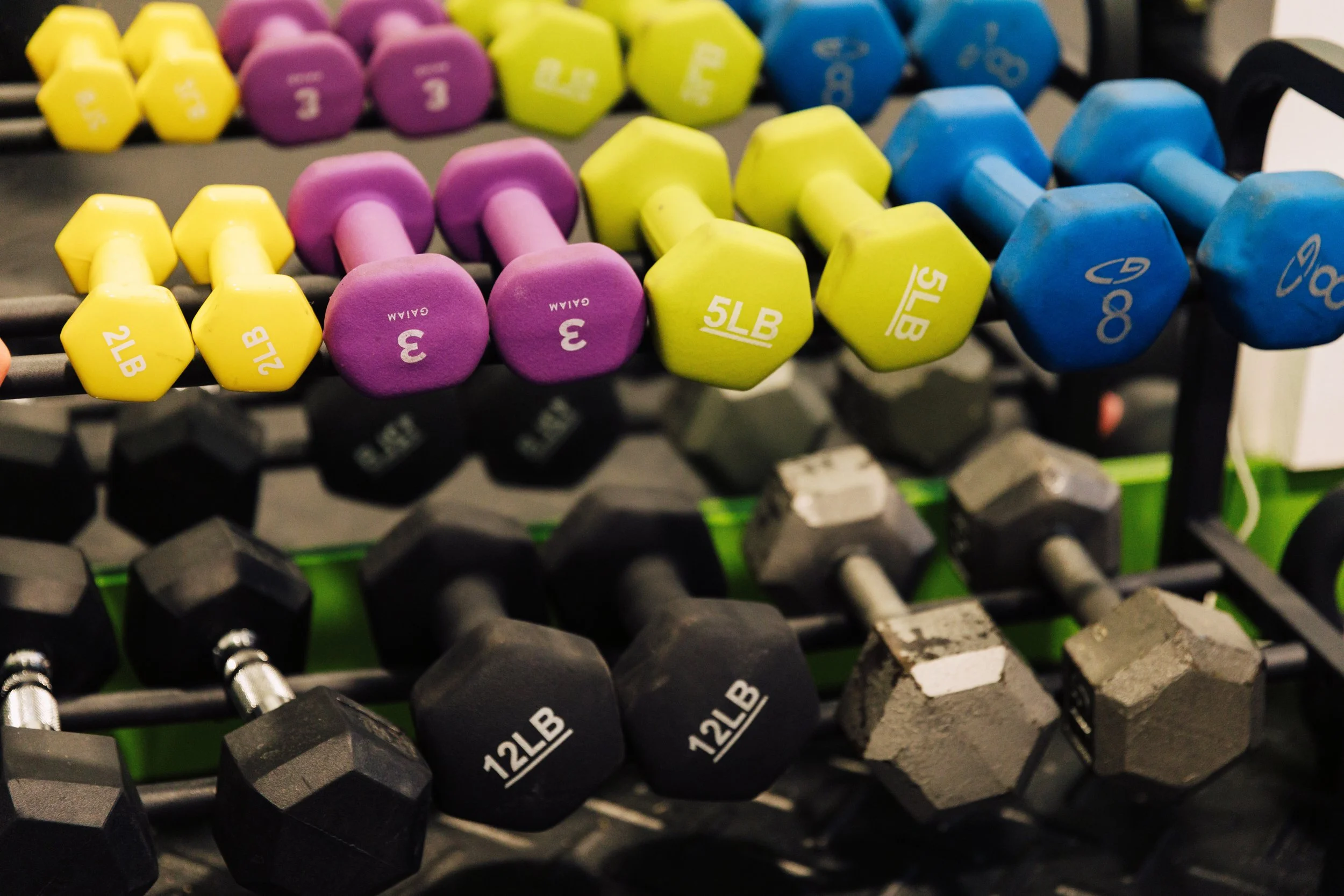 Close-up of yellow running shoes, a black dumbbell, and an SOS fitness weight plate in a gym.