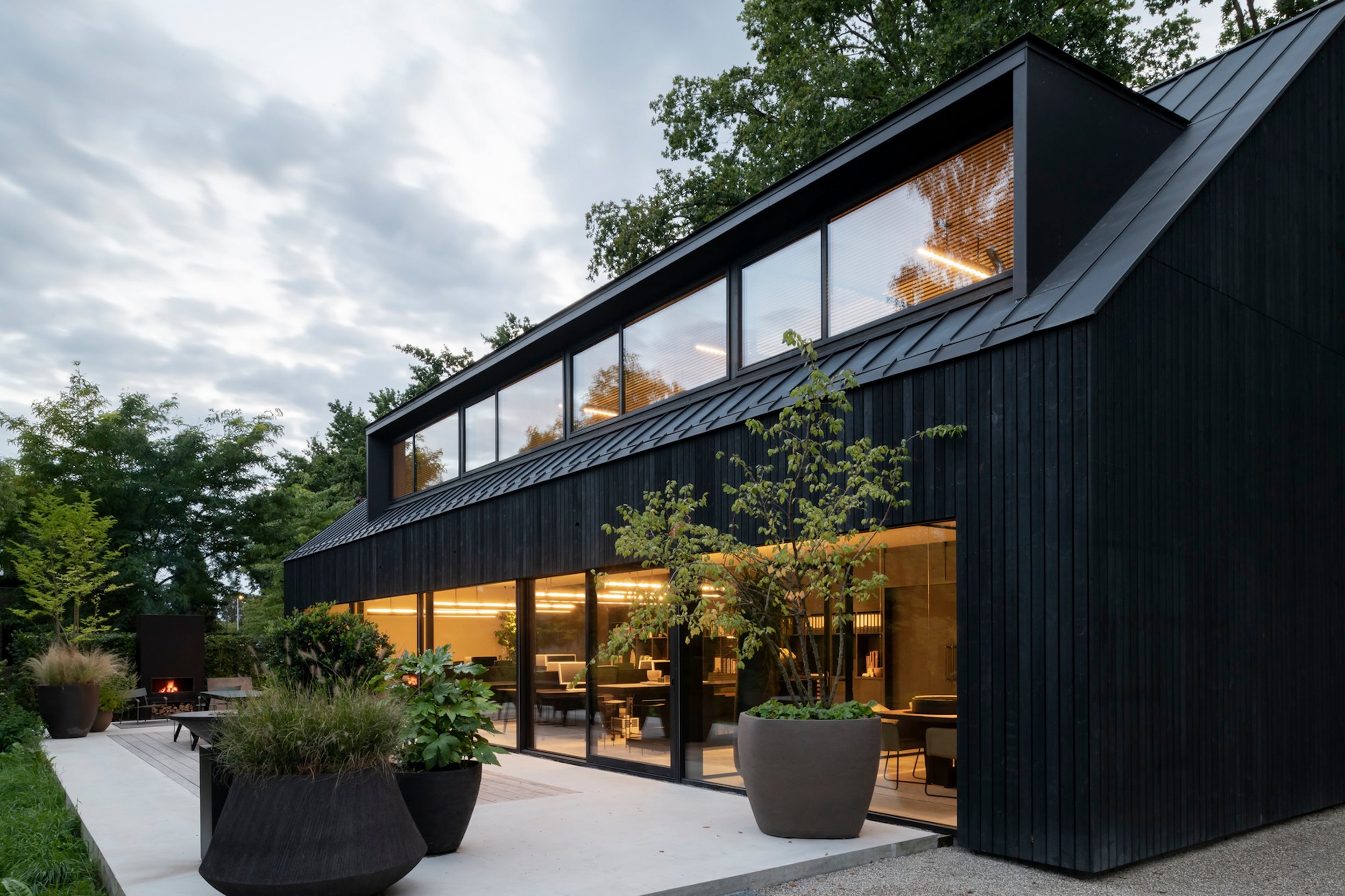 Contemporary black timber-clad house featuring expansive glass windows, sharp roof lines, and landscaped outdoor seating, a modern commercial design that blends architectural elegance with natural surroundings