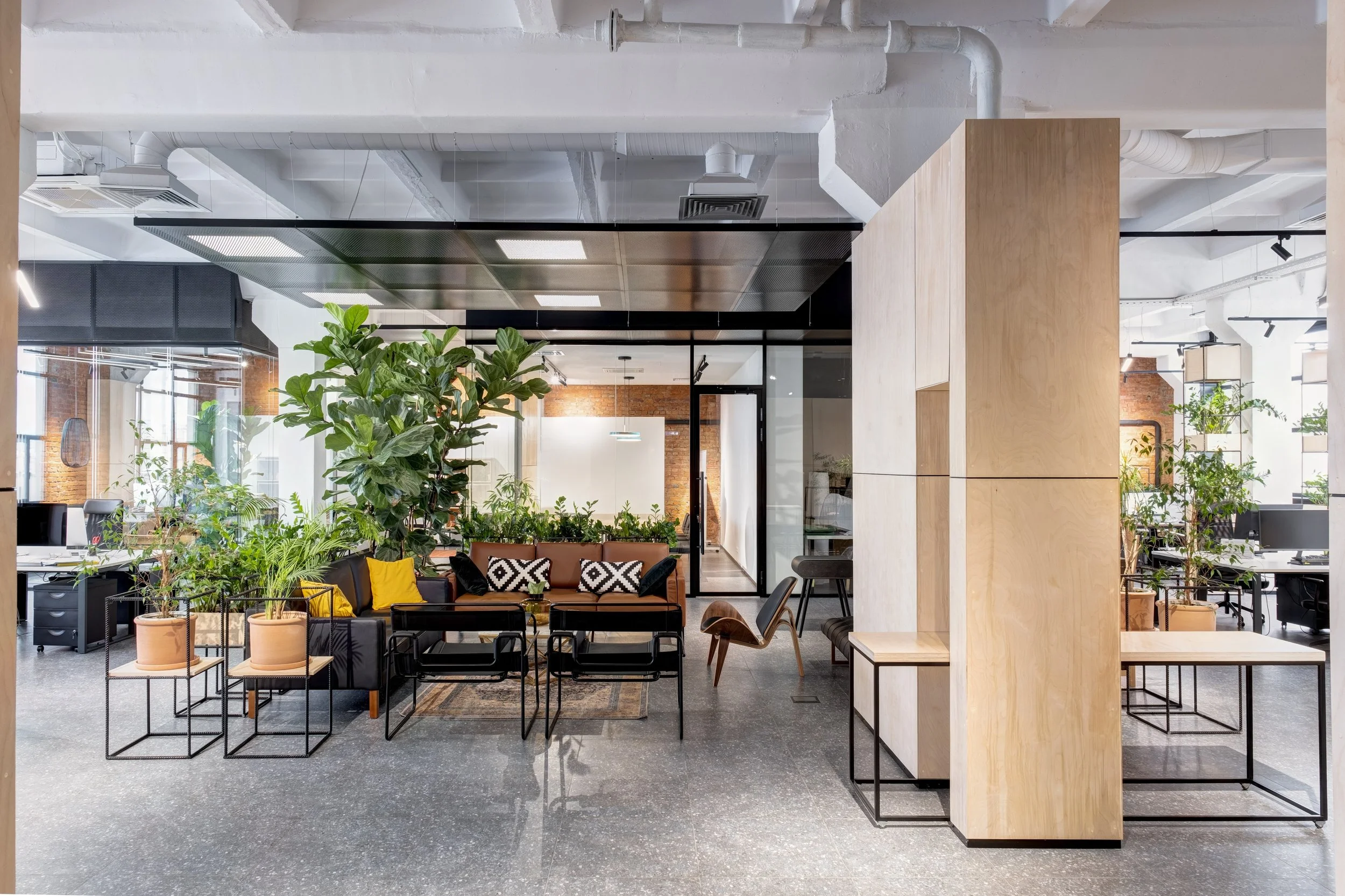 Modern commercial office interior with indoor plants, collaborative seating, glass meeting rooms and contemporary workspace design.